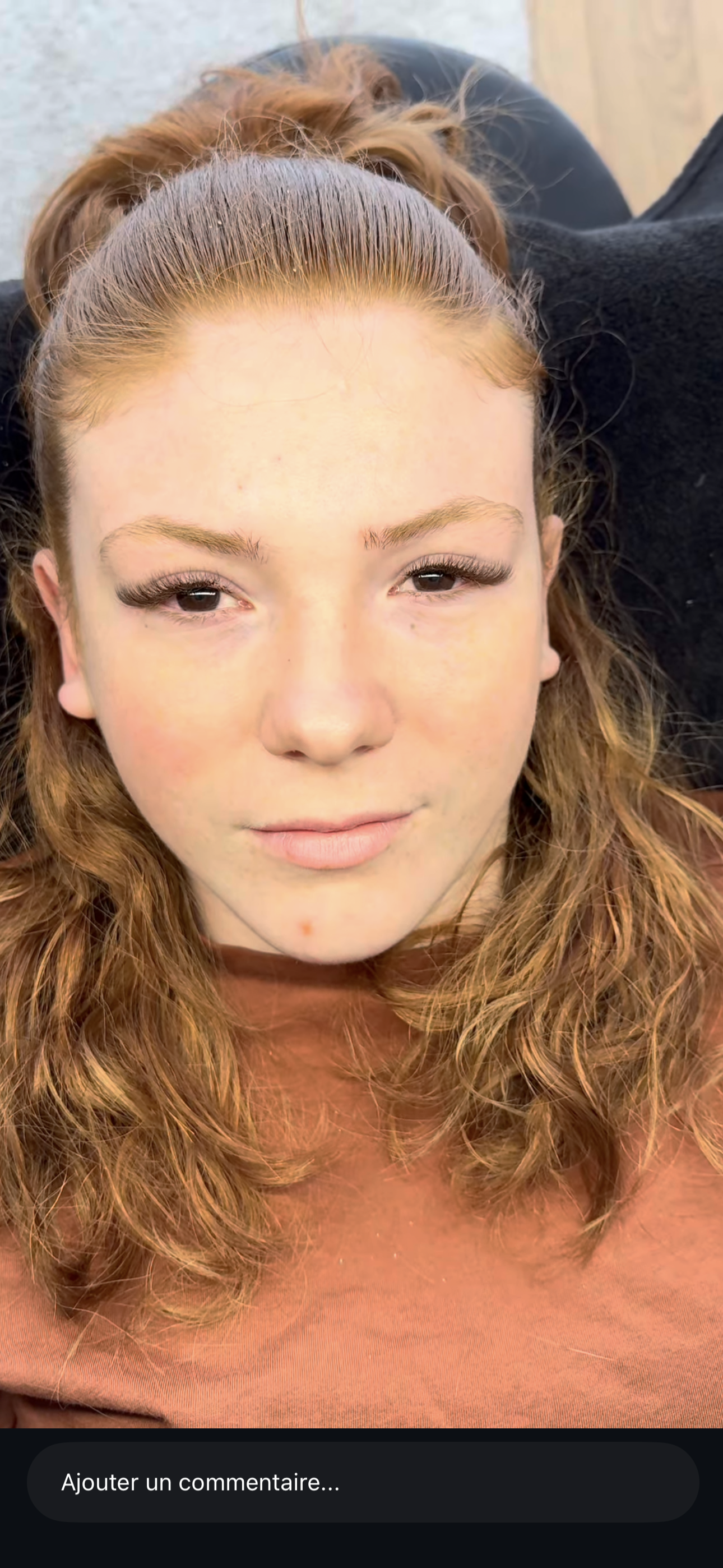 Une jeune femme aux cheveux roux, yeux marron et maquillage léger, regardant directement la caméra, avec un coussin noir derrière elle.