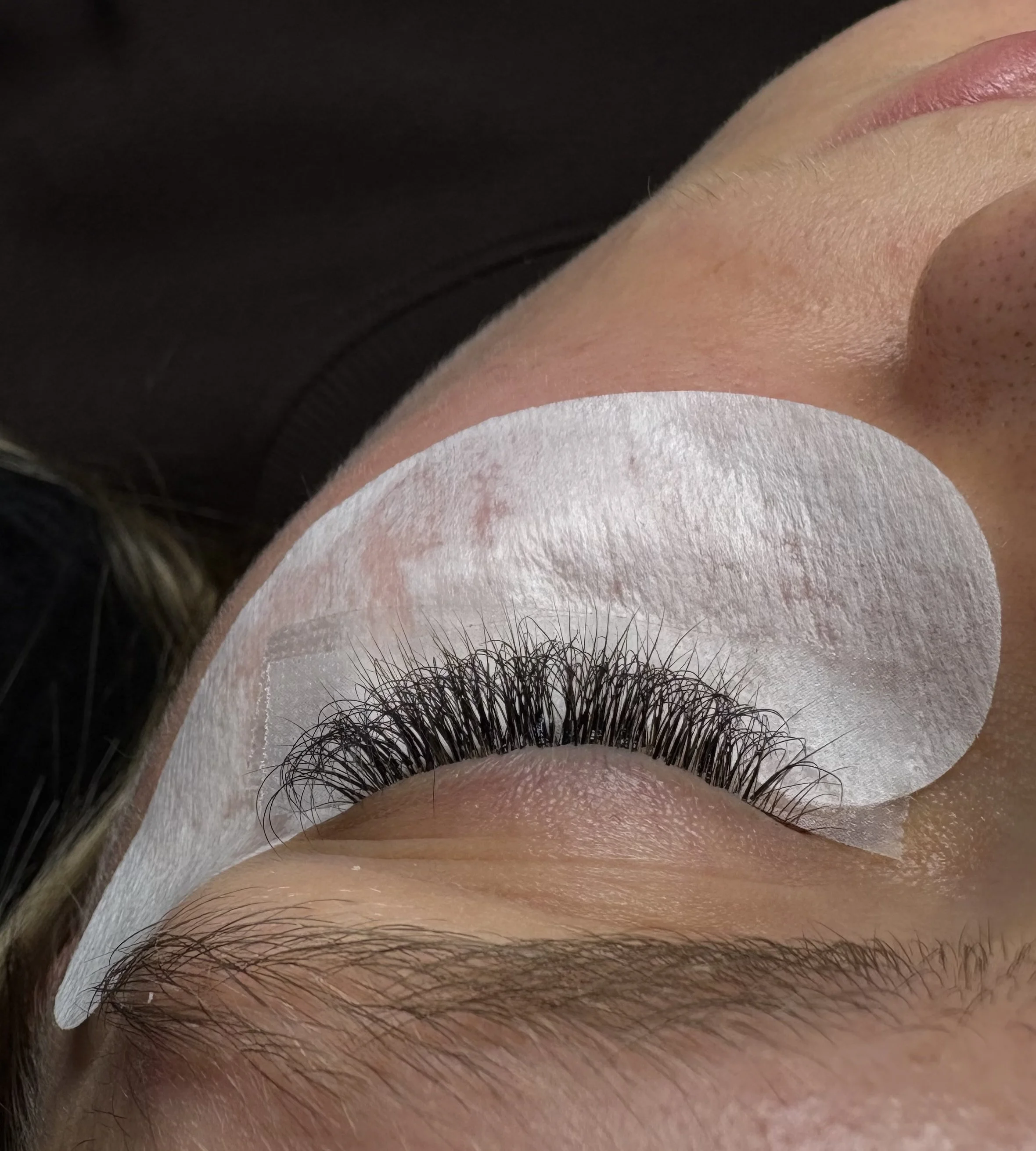 C'est une image de yeux fermés avec des cils longs et des sourcils bien définis, un fond blanc et une présence de maquillage ou de produit sur la peau autour de l'œil.