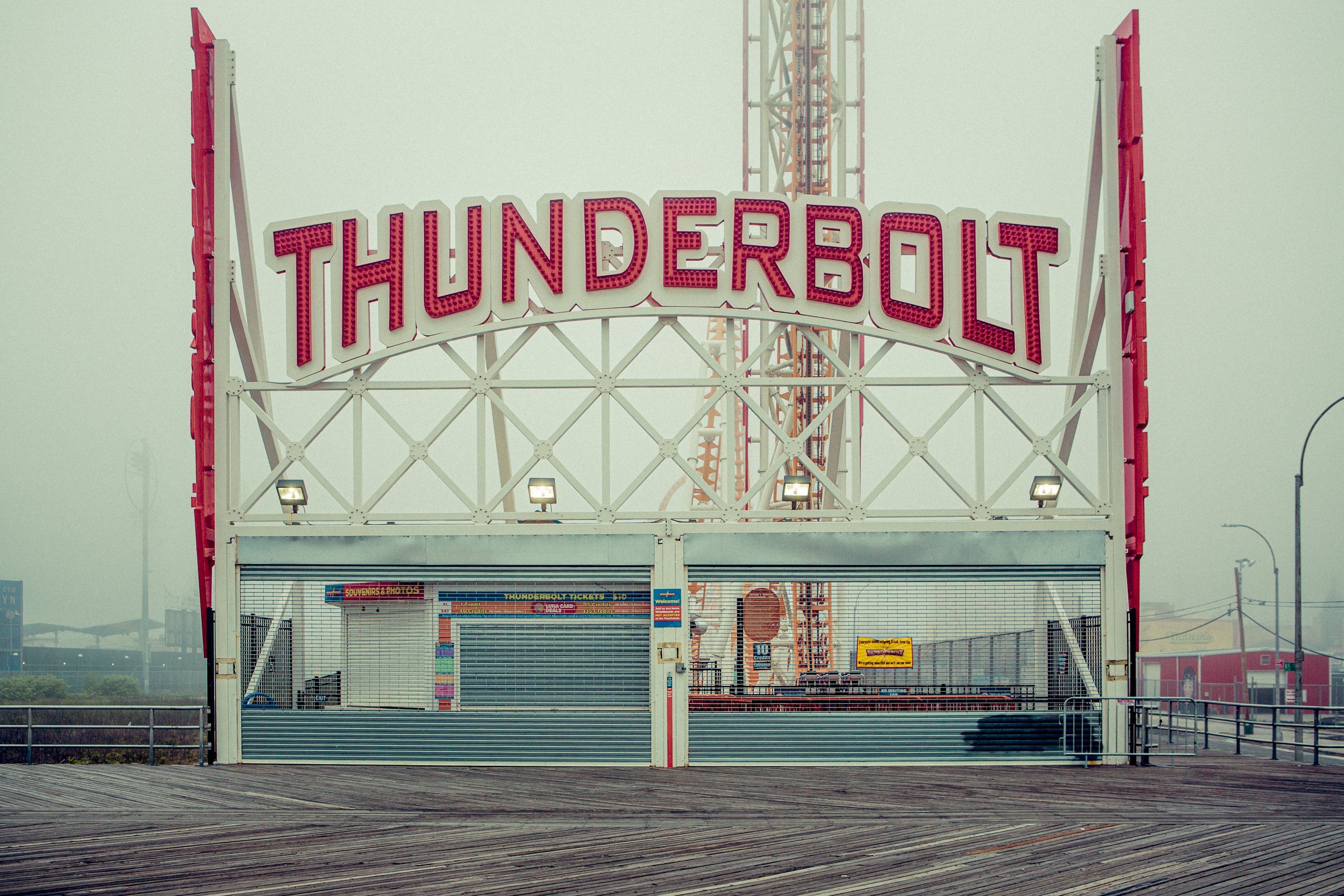 Une entrée d'attraction appelée Thunderbolt avec un panneau lumineux rouge et une file d'attente vide devant. Atmosphère brumeuse ou venteuse