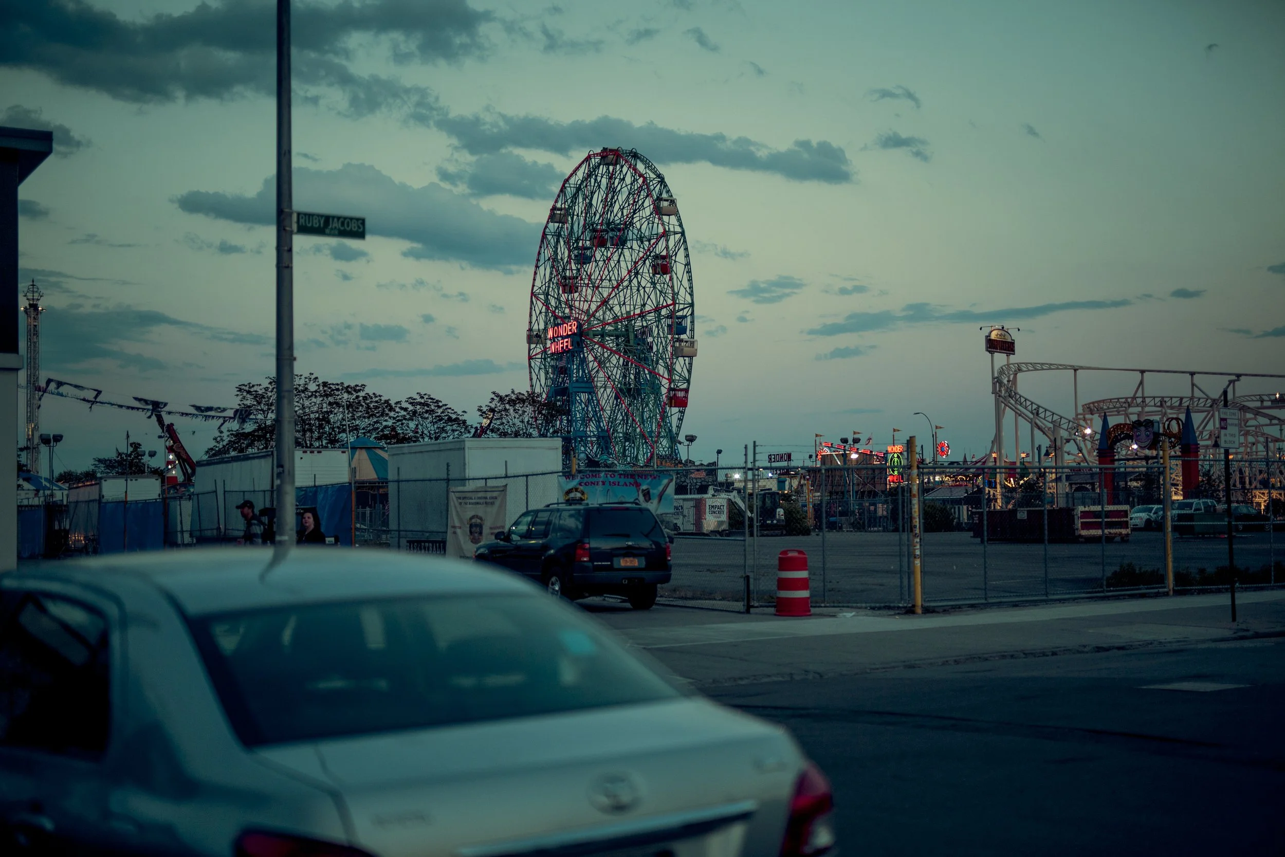 Une grande roue d'attraction au parc d'attractions Wonder Wheel avec un ciel nuageux en arrière-plan, entourée de voitures et de structures de fête dans une scène urbaine ou de parc d'attractions.