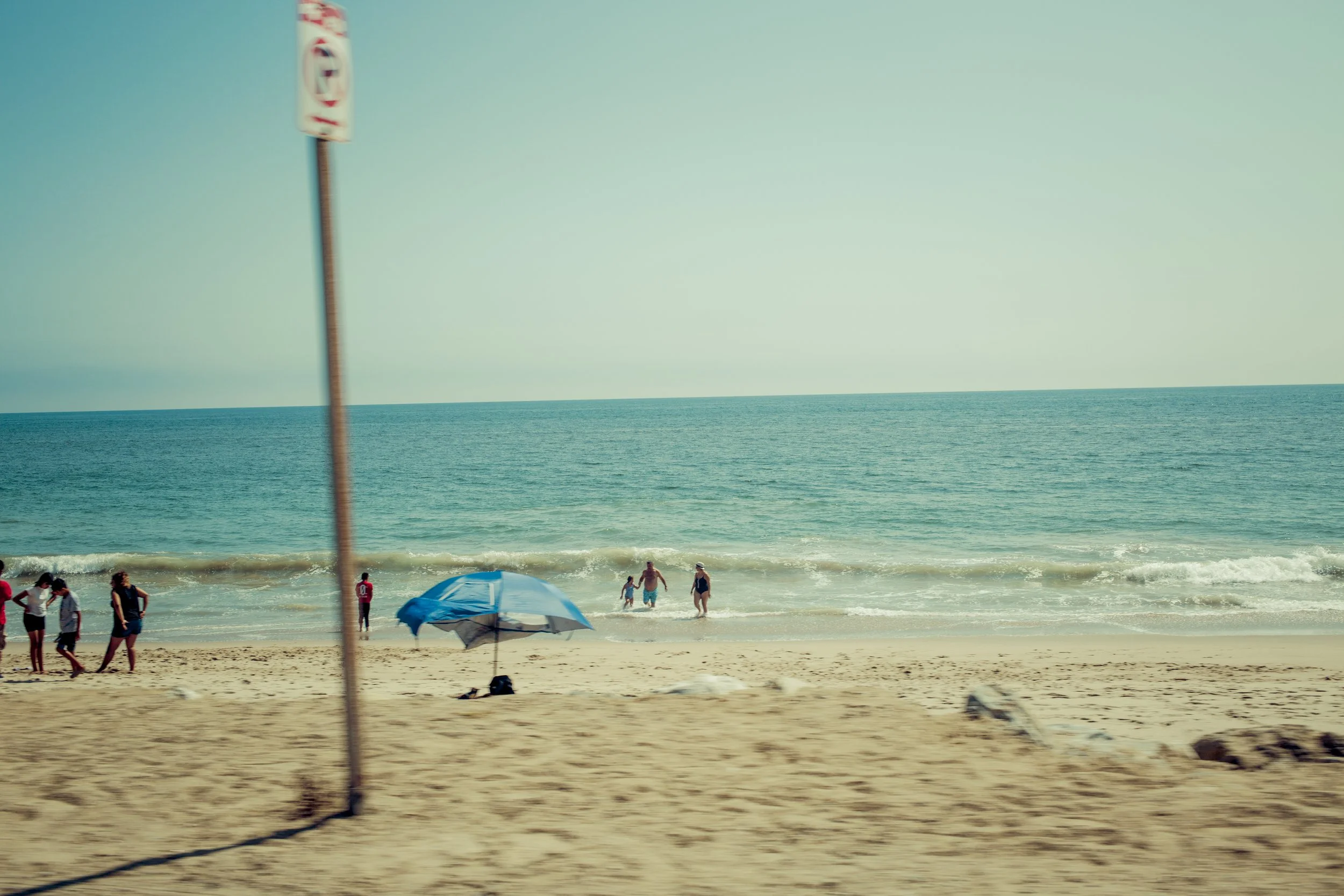 Plage avec des personnes nageant et se relaxant près de la mer, parasols bleus et un ciel clair