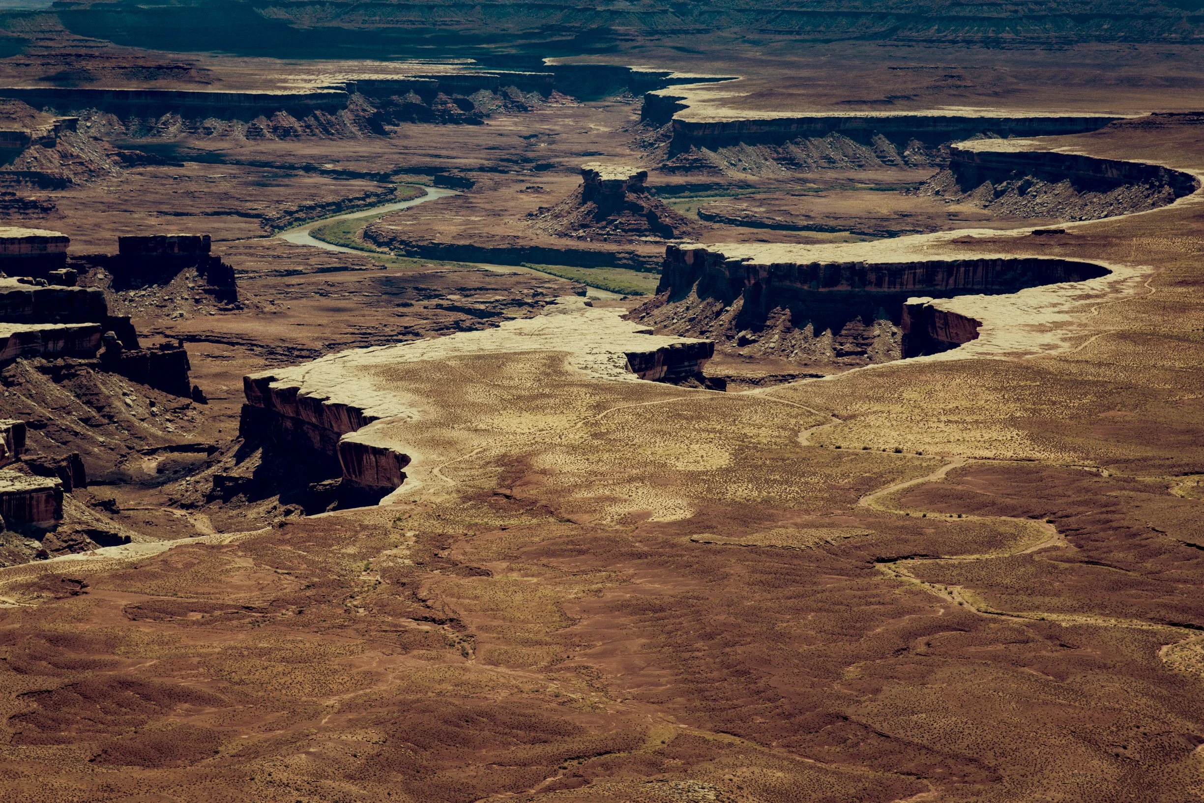 Canyon aride avec un fleuve serpentant au fond. Des formations rocheuses érodées par le vent et la pluie dominent le paysage.