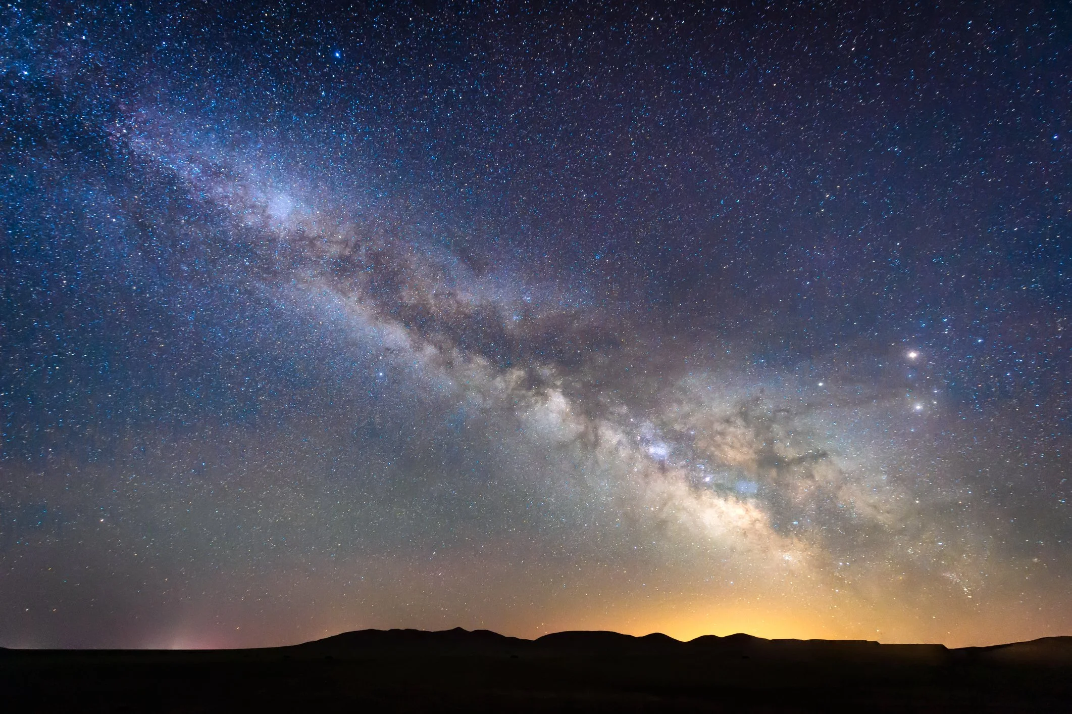 A clear night sky filled with countless stars and the Milky Way galaxy visible above a silhouette of mountains or hills.