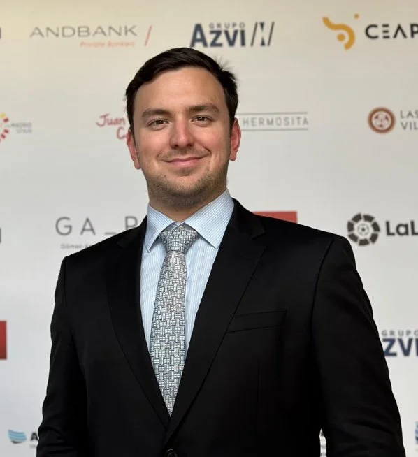 Hombre con traje y corbata en un evento con fondo de logos y marcas