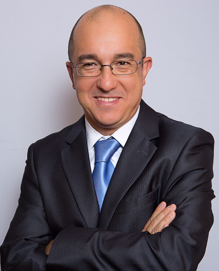 Hombre de negocios con gafas, vestido con saco y corbata, sonriendo con los brazos cruzados.