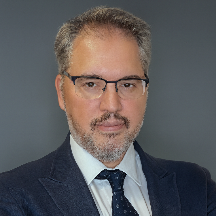 Retrato de un hombre con gafas, barba y cabello peinado, vestido con saco y corbata en un fondo gris.