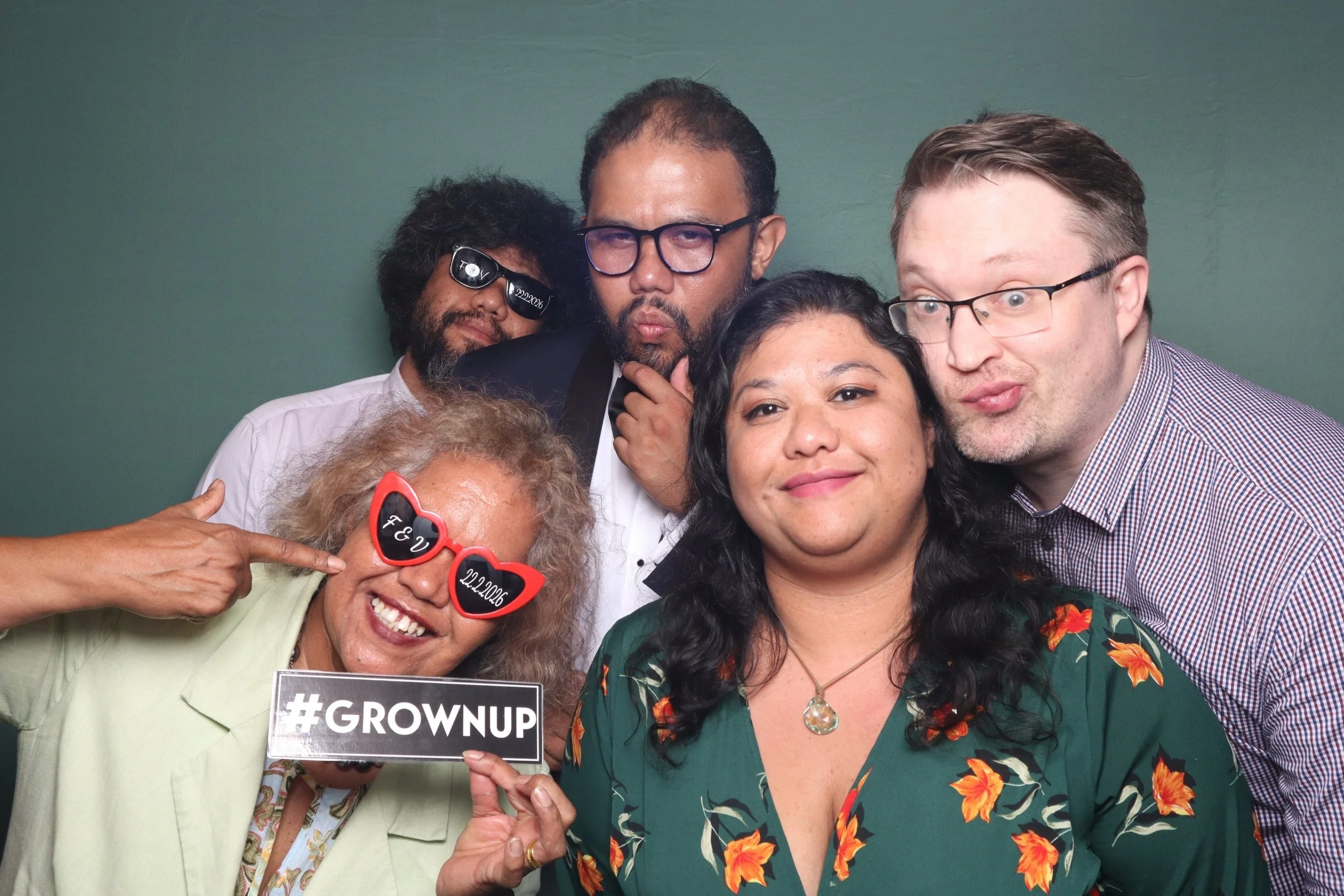 Group of five guests including a groomposing together in front of the moderm led photobooth.  Wedding setup at bookbarn in central coast with a garden theme hence the green backdrop and customised props.