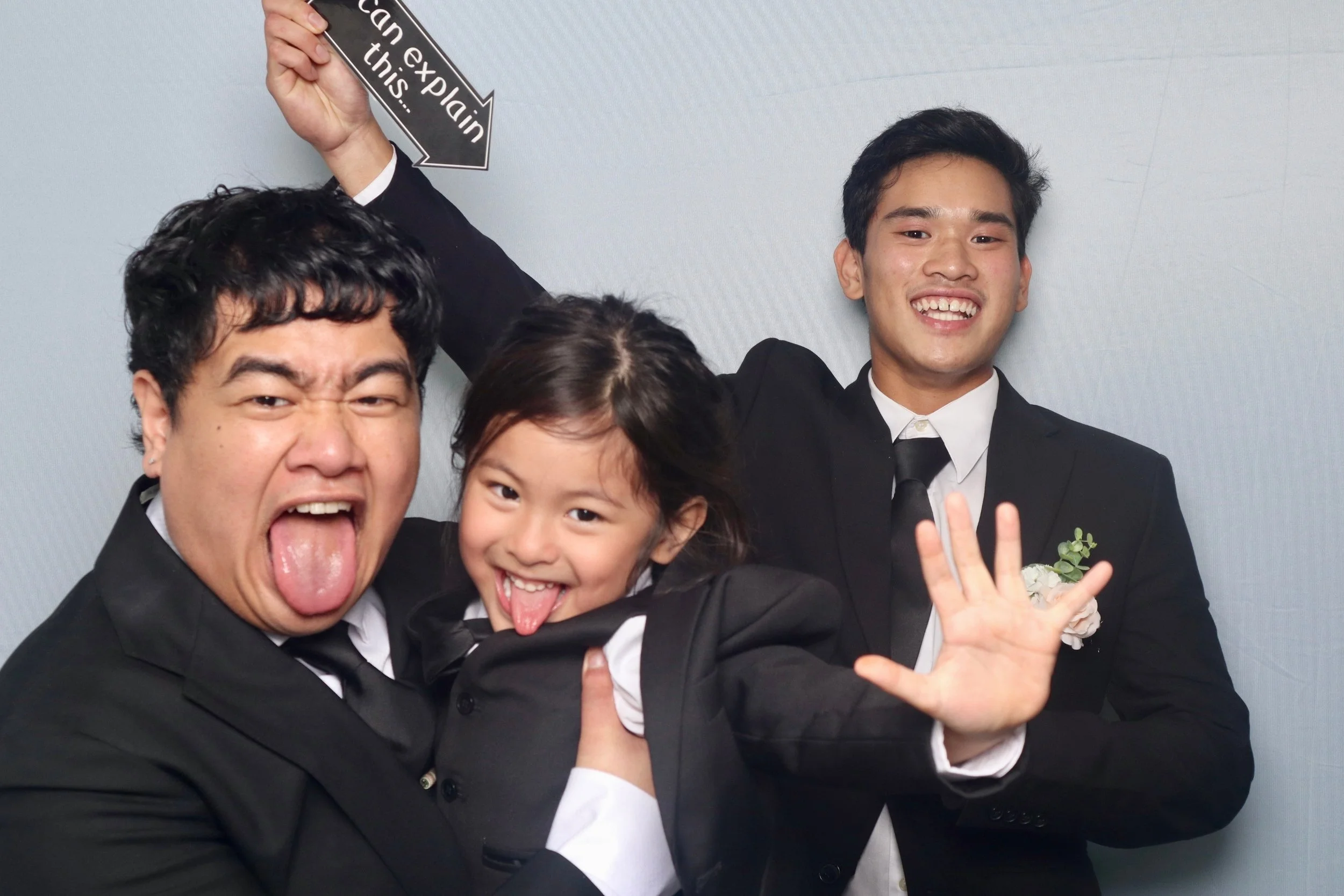A group of young guests two men ang a boy ringbearer dressed in formal black tuxedos posing cute and playful in front of the luxury photobooth. They are making silly faces and gestures enough to cap the wedding night. 