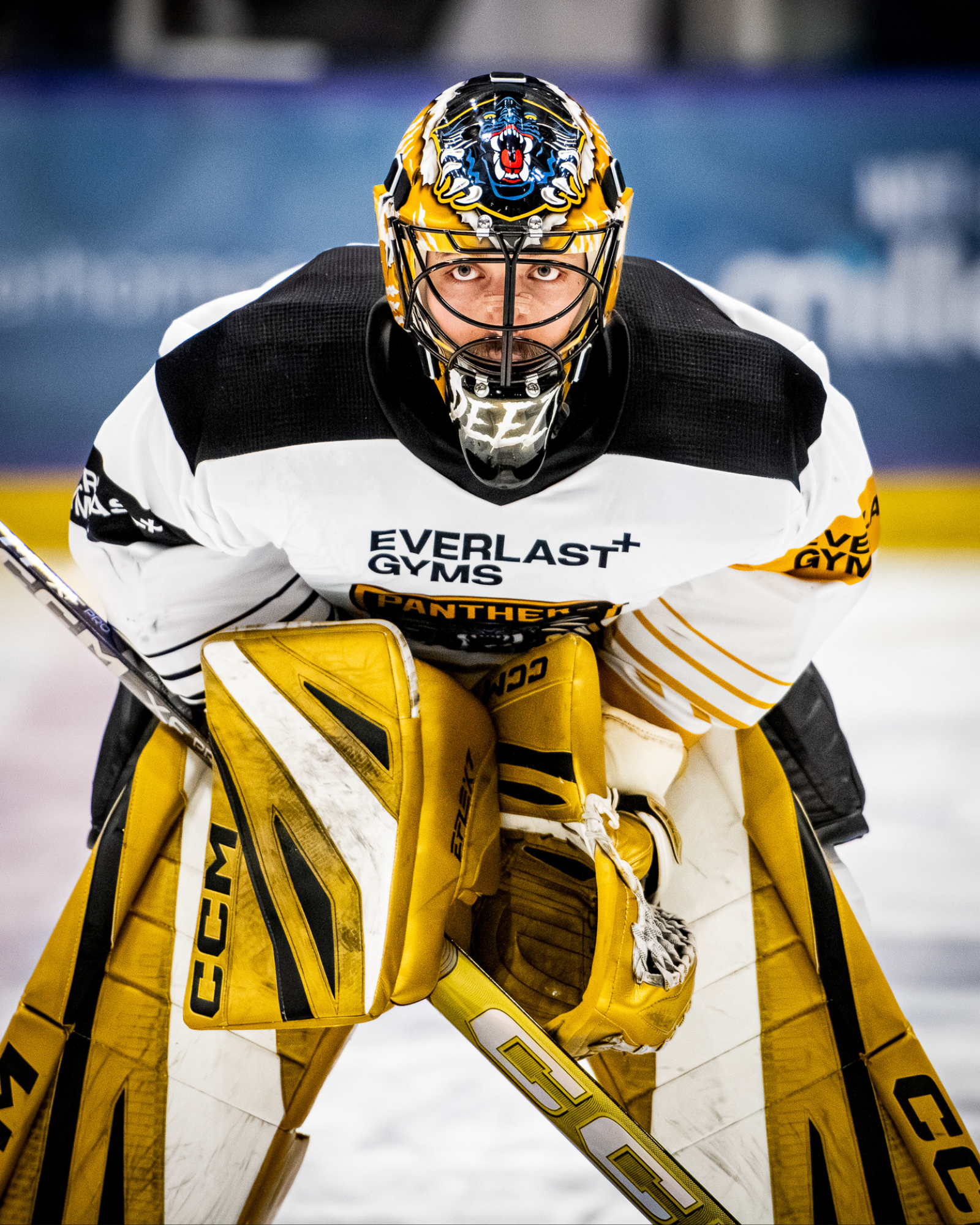 Hockey goalie wearing a black and white jersey with yellow pads, mask featuring a panther logo, and focused on the game.