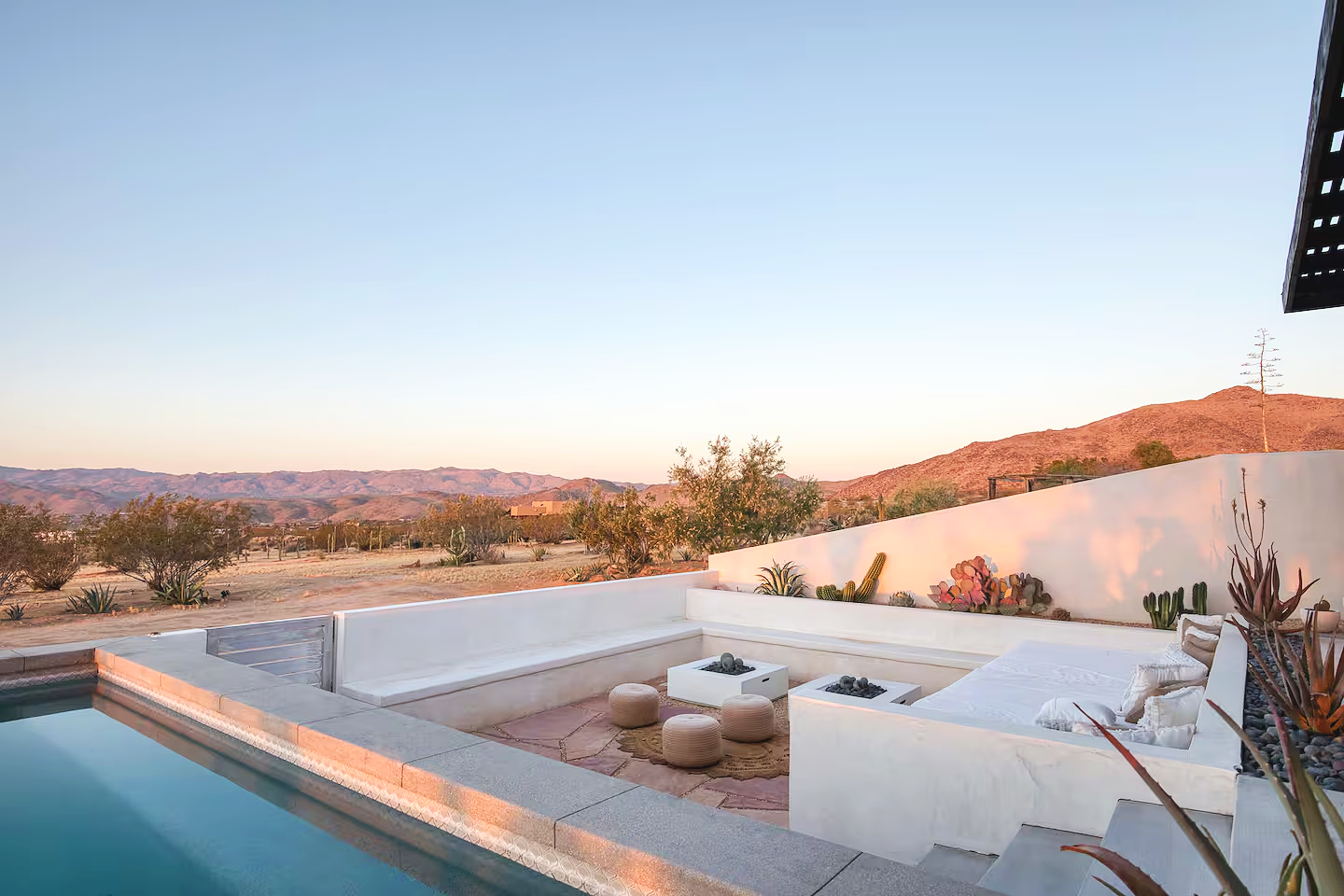 Luxury outdoor pool and seating area with desert landscape and mountains in the background at sunset.