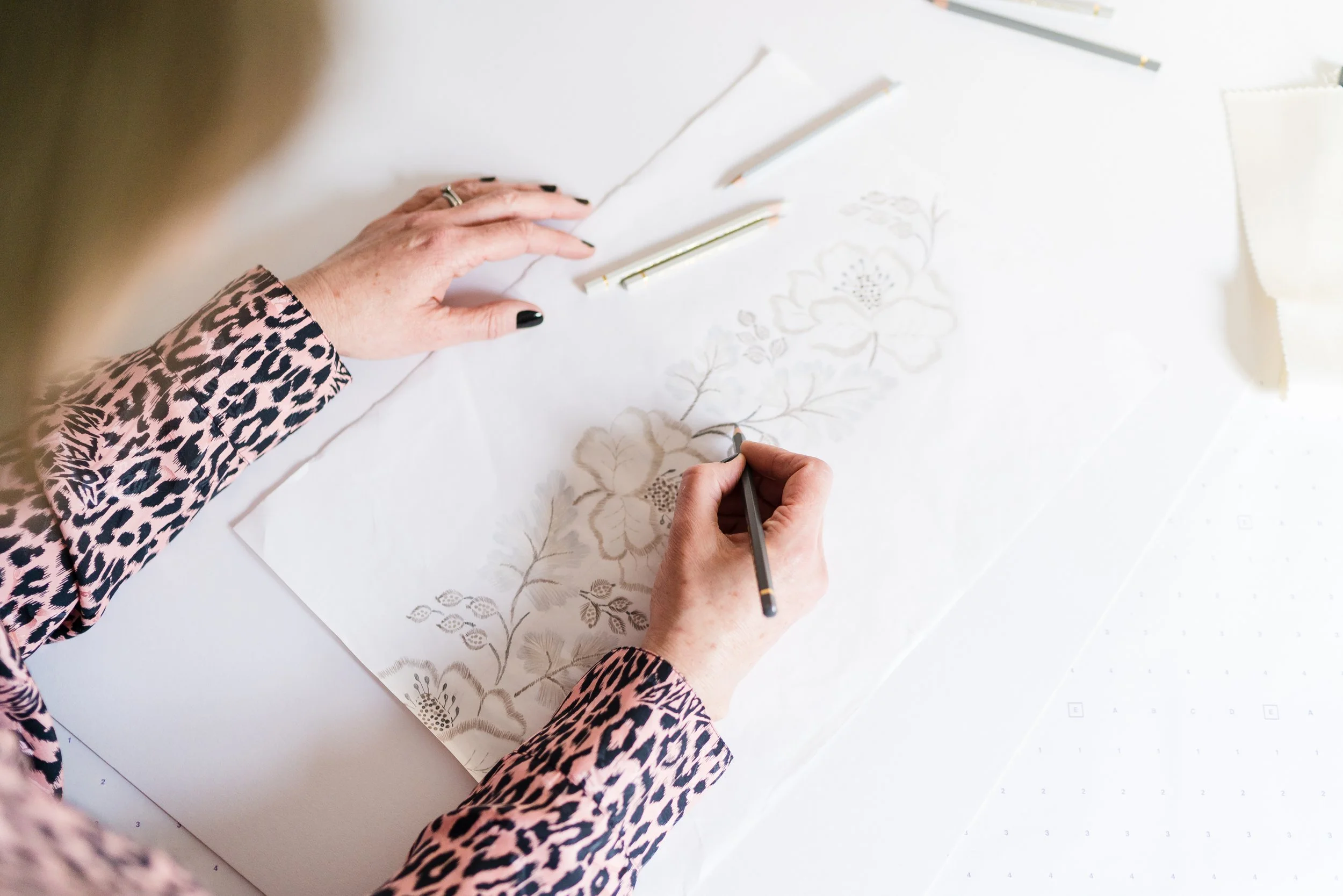 Person working on detailed floral embroidery design on large fabric sheet with colored pencils and markers.