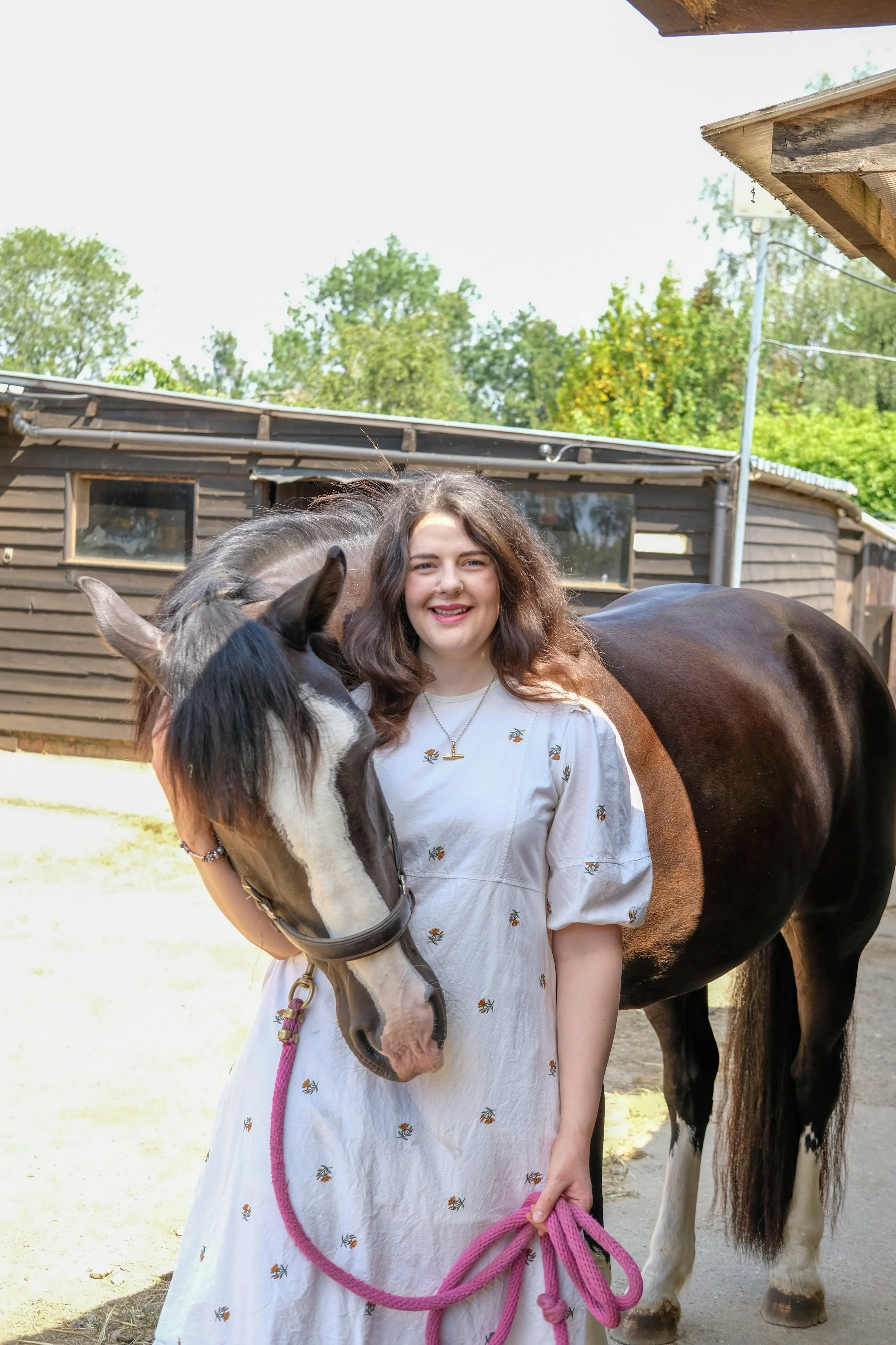 Bethany Stone wearing a floral dress and stood with a bay horse with a white blaze