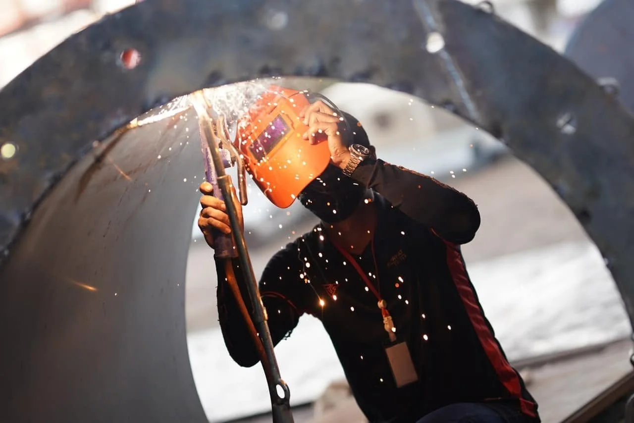 A worker welding inside a large metal pipe, sparks flying while wearing protective gear.
