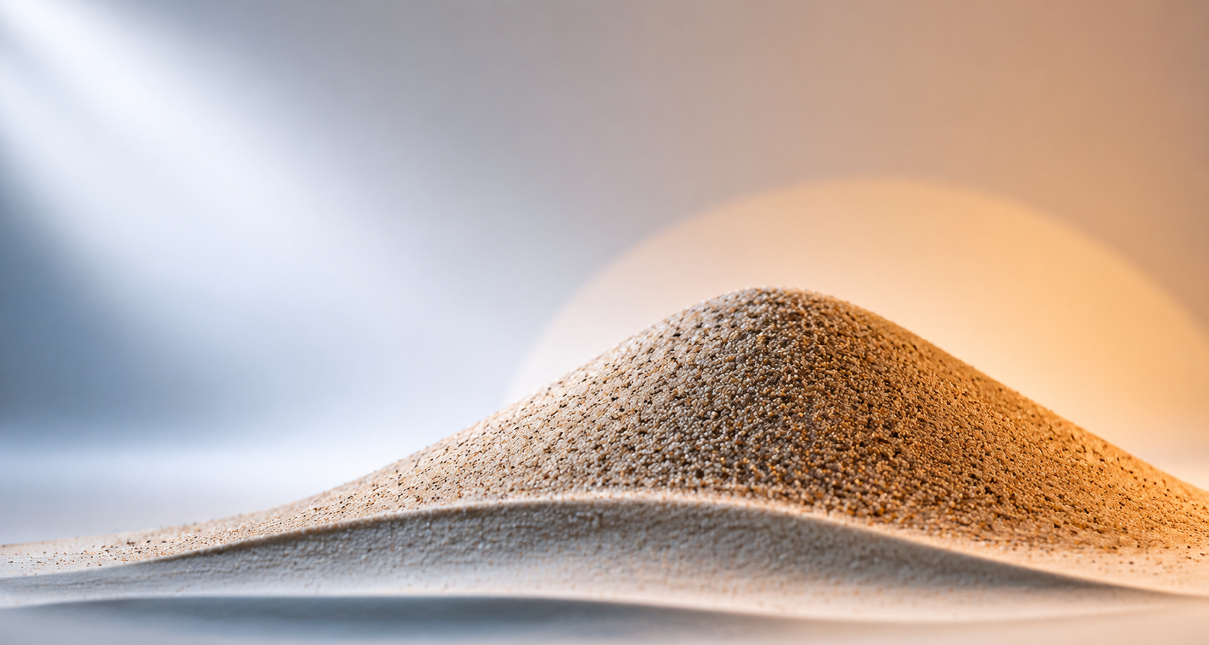 Close-up of a small sand dune with fine grains, against a blurred background with soft lighting.