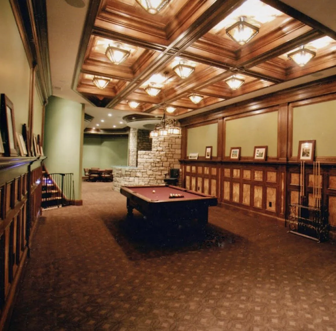 An elegant game room with a pool table, wood-paneled walls, and a coffered ceiling with warm lighting.