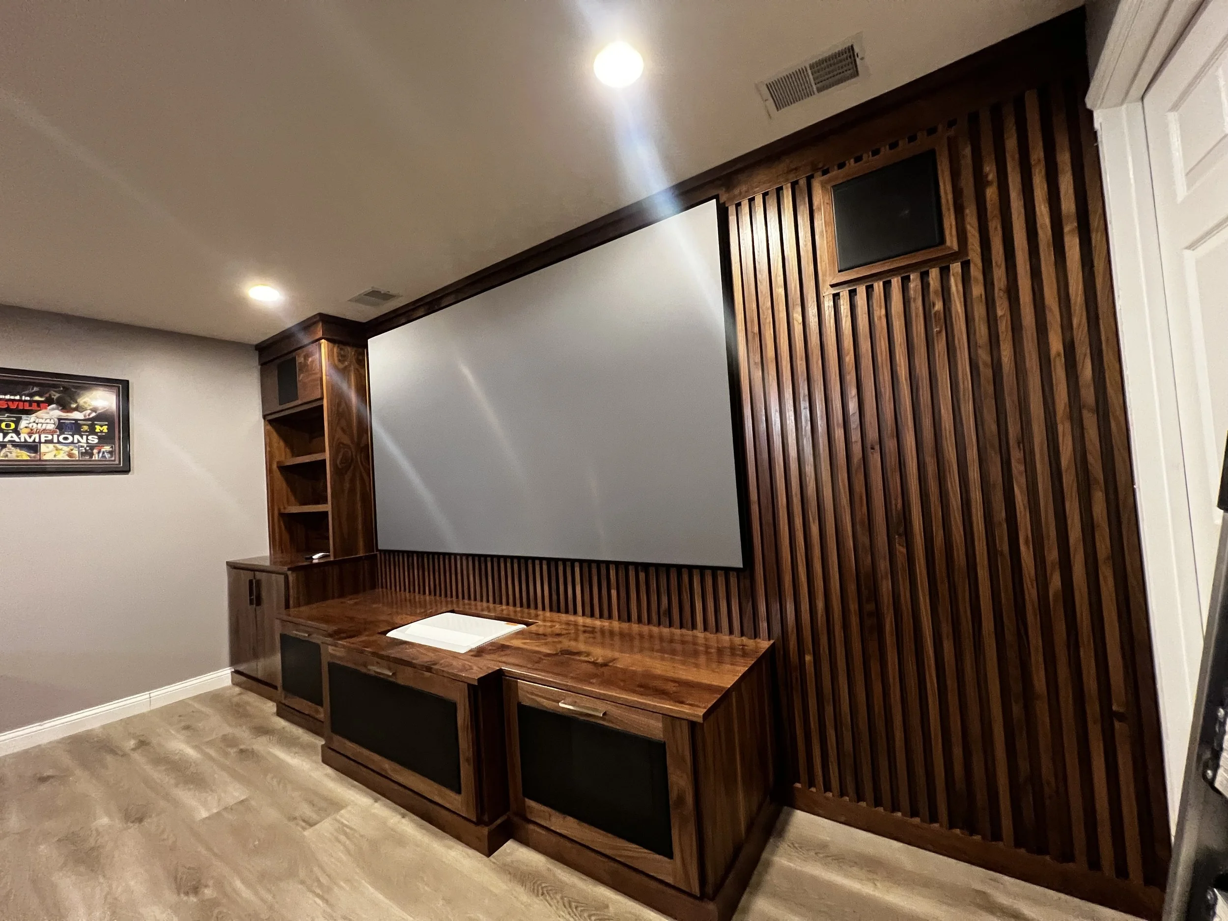 Living room featuring a custom wood entertainment center with integrated paneling, housing a projection screen and wall-mounted speakers, emphasizing tailored wood craftsmanship and architectural detailing along the feature wall.