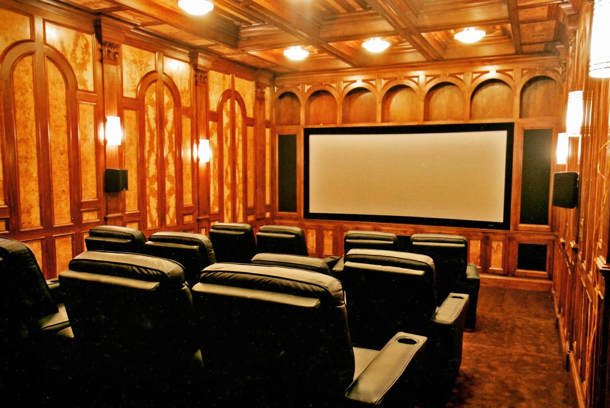 Fully custom home theater featuring rich wood-paneled walls and a detailed coffered wood ceiling, designed to frame a projection screen and create a warm, immersive viewing environment with integrated architectural lighting.