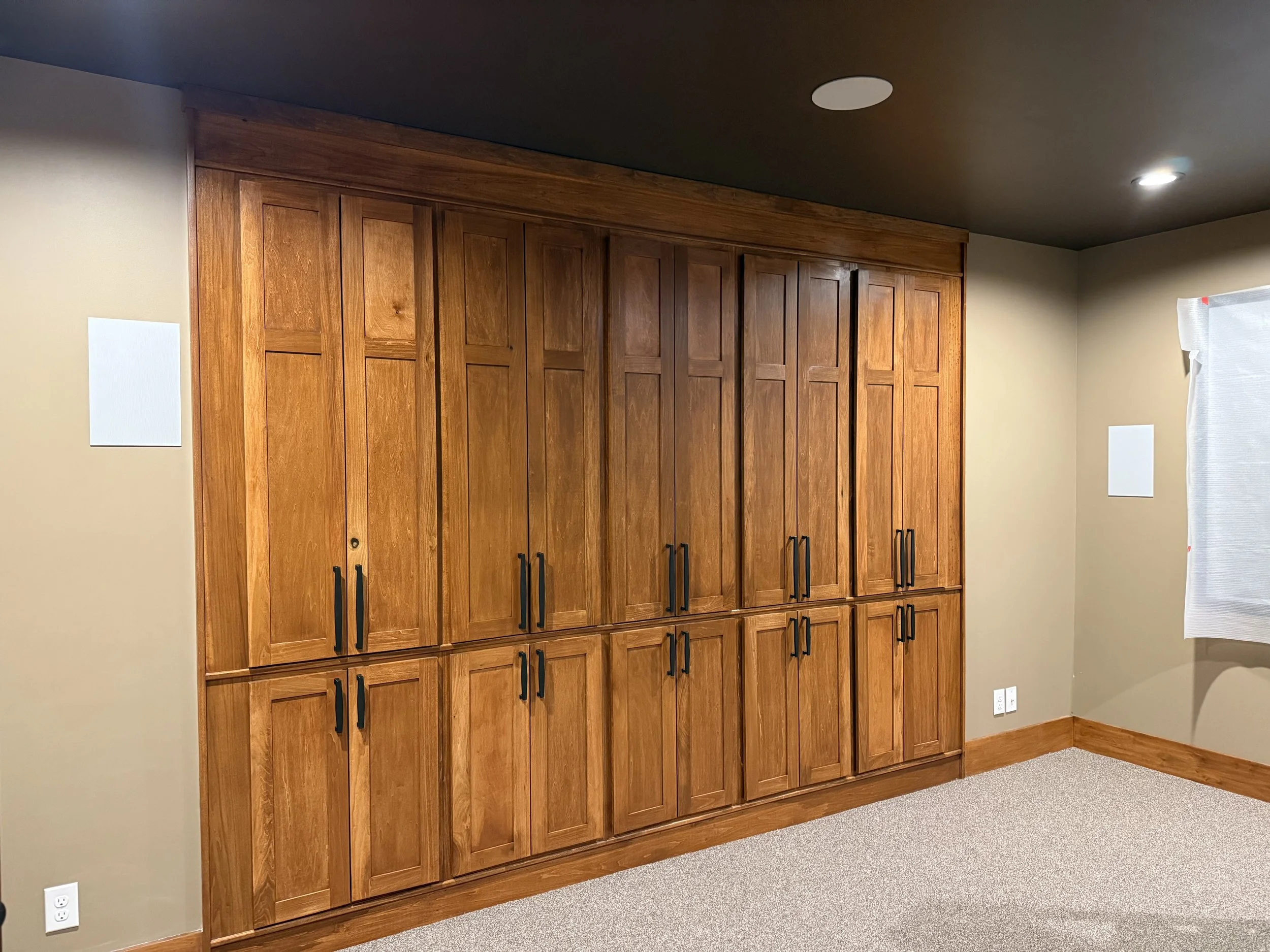 Room featuring a wall of custom-built wood cabinets with full-height doors and contrasting dark hardware, designed as integrated wall storage that emphasizes clean lines, craftsmanship, and efficient use of space.