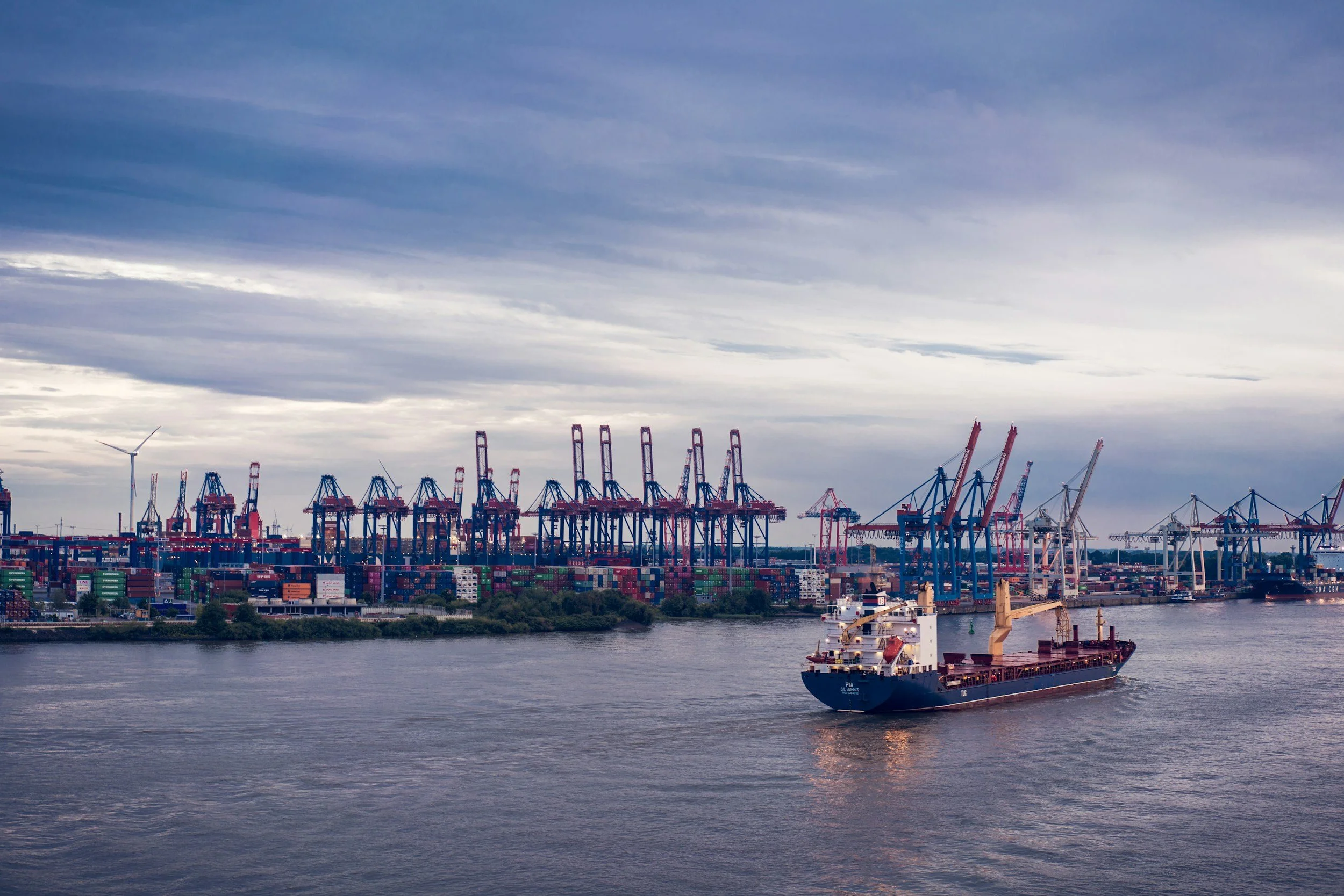 A port with container ships and cranes under a cloudy sky.