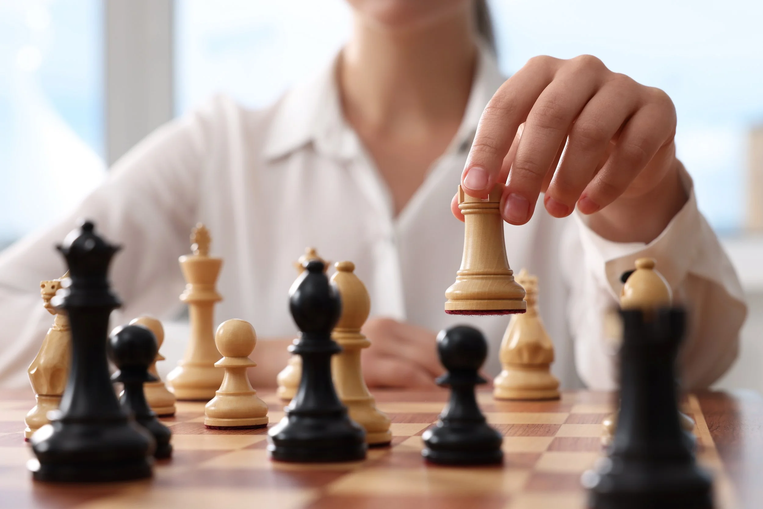 A person in a white shirt playing chess, moving a light-colored rook on a chessboard.