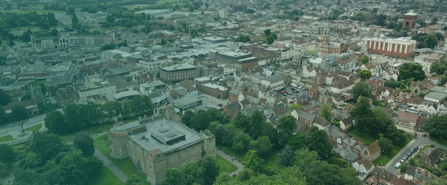 Aerial view of a small town with a historic stone castle surrounded by green trees and residential houses