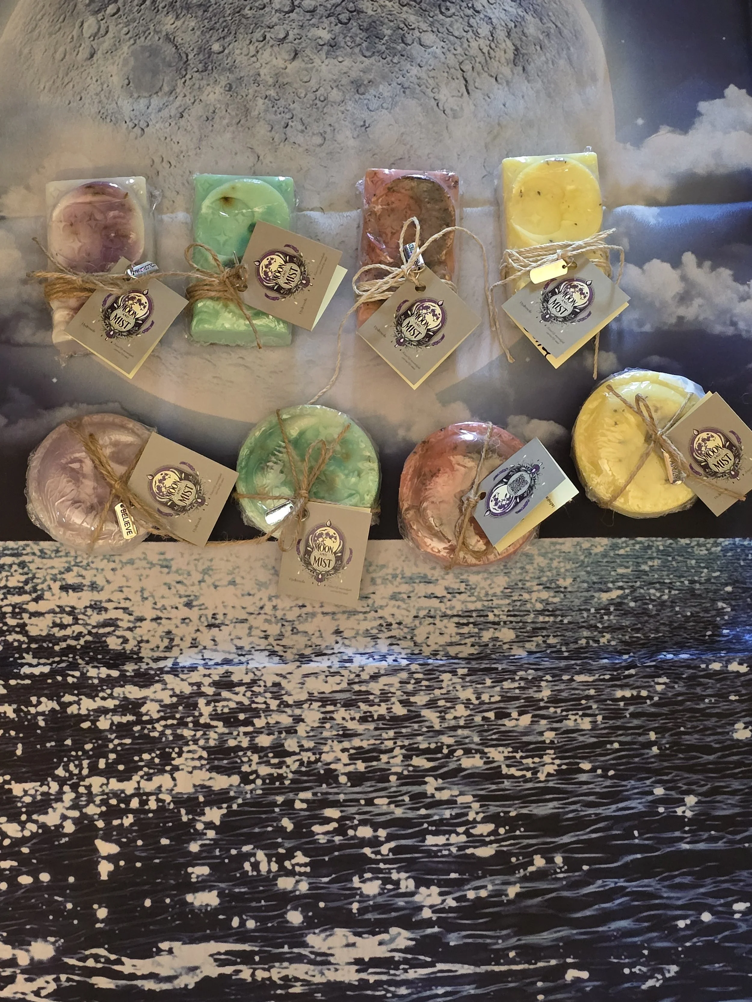 Various colorful candles with tags and twine on a surface with a moon and clouds background.