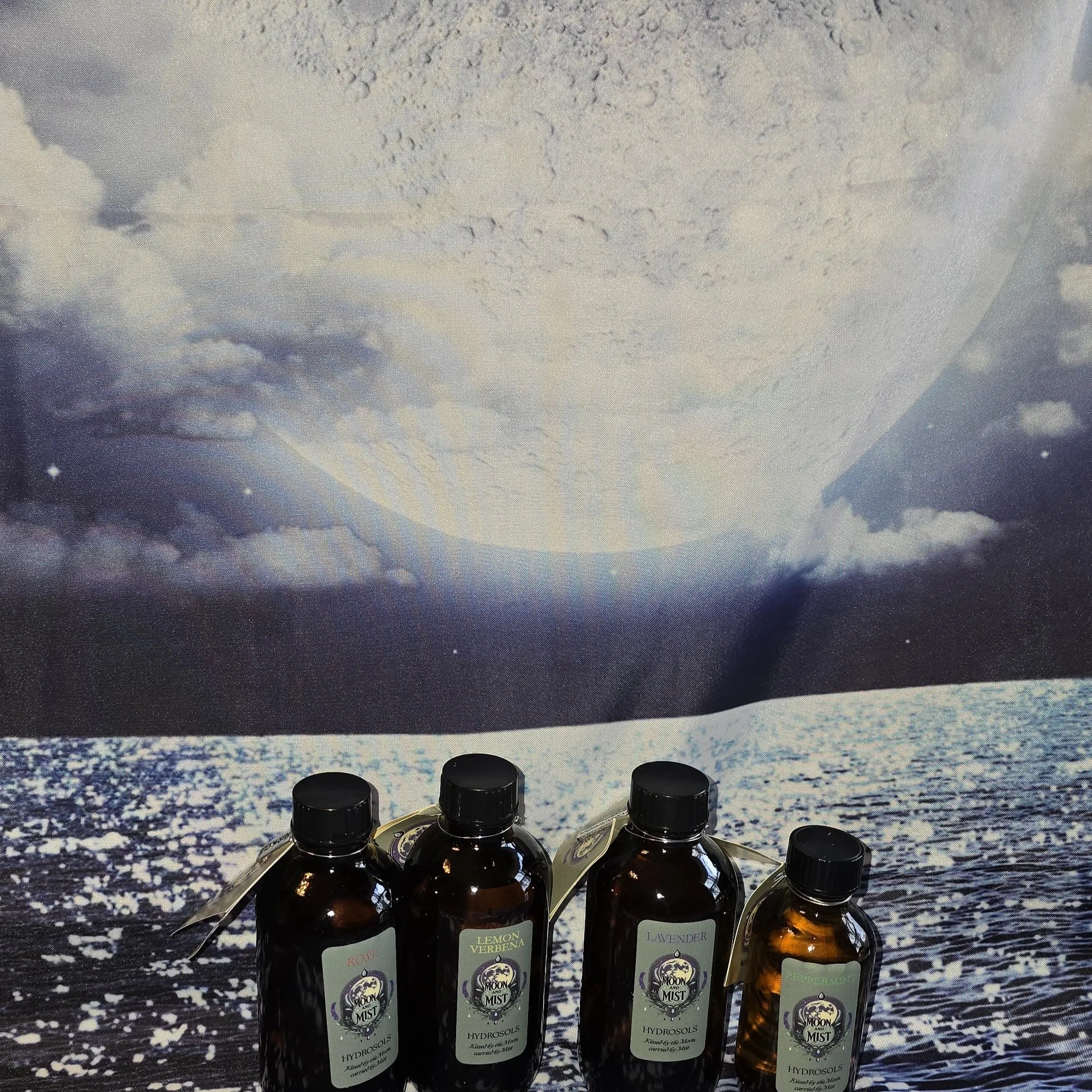 A row of brown glass bottles labeled with different essential oils, set against a background of a large, cloudy sky over an ocean or beach scene.