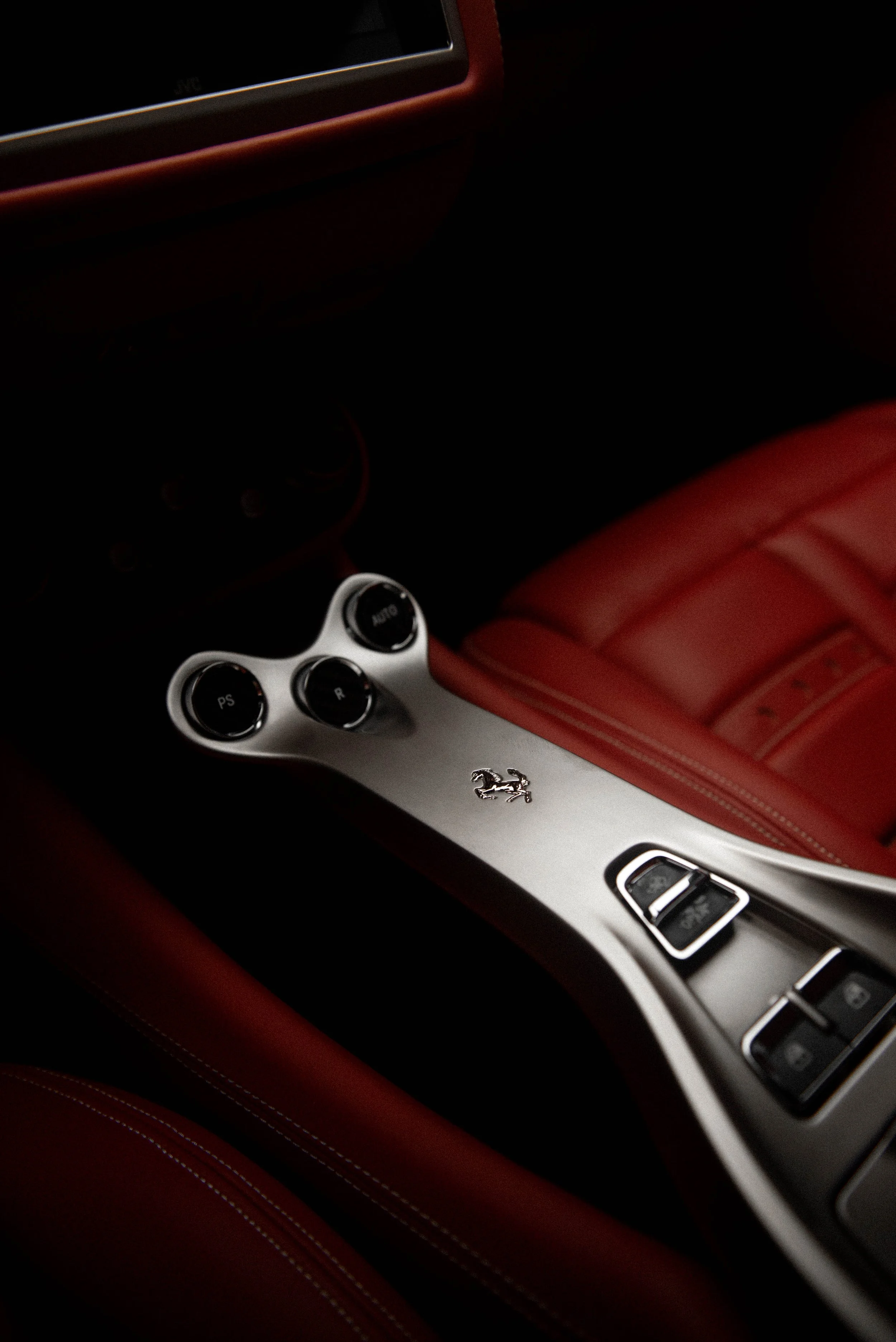Close-up of a car interior showcasing red leather seats, a metal center console with control buttons, and a Ferrari logo.