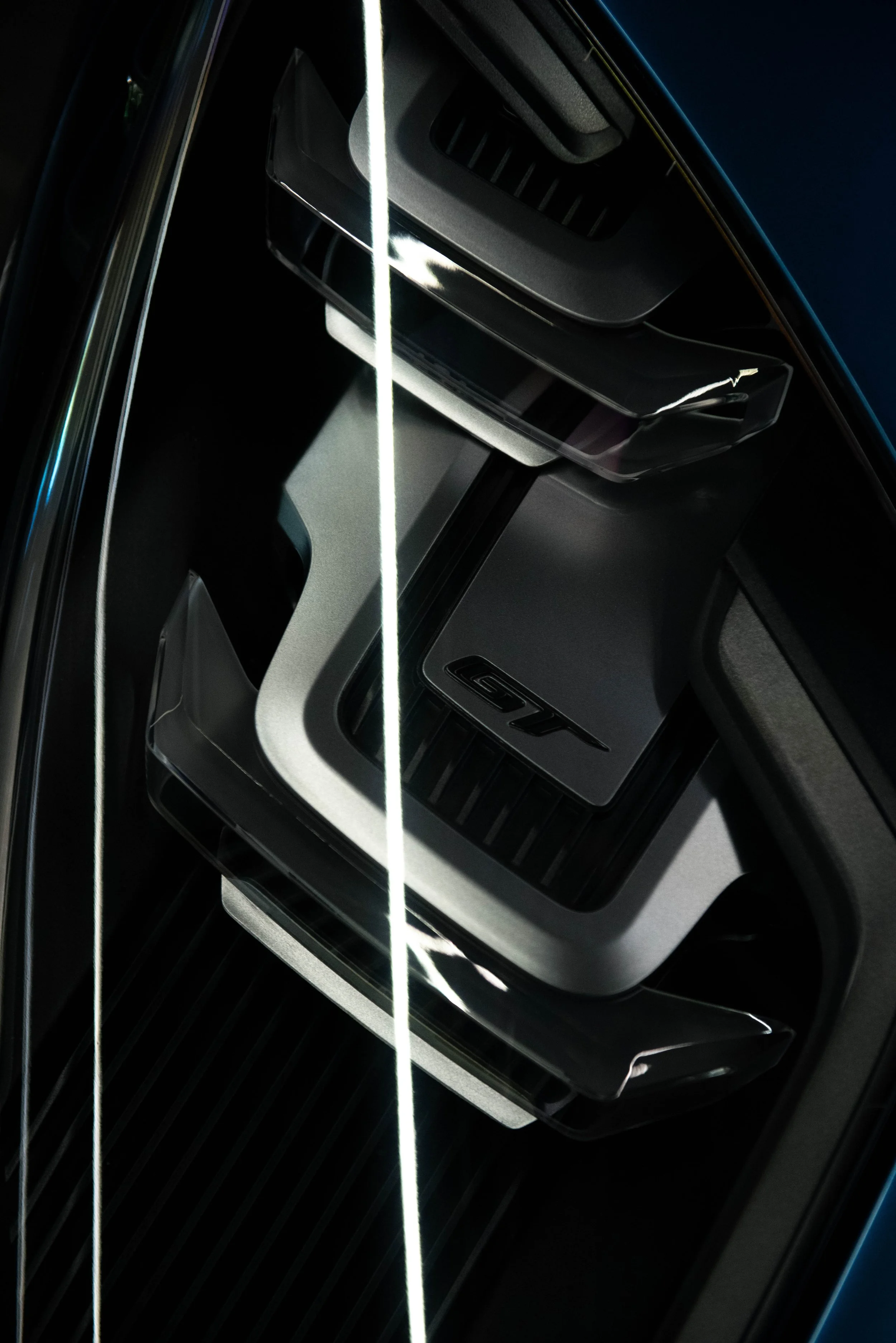 Close-up of a car's front grille with a shiny, black surface and blade-style horizontal slats, partially reflecting light.