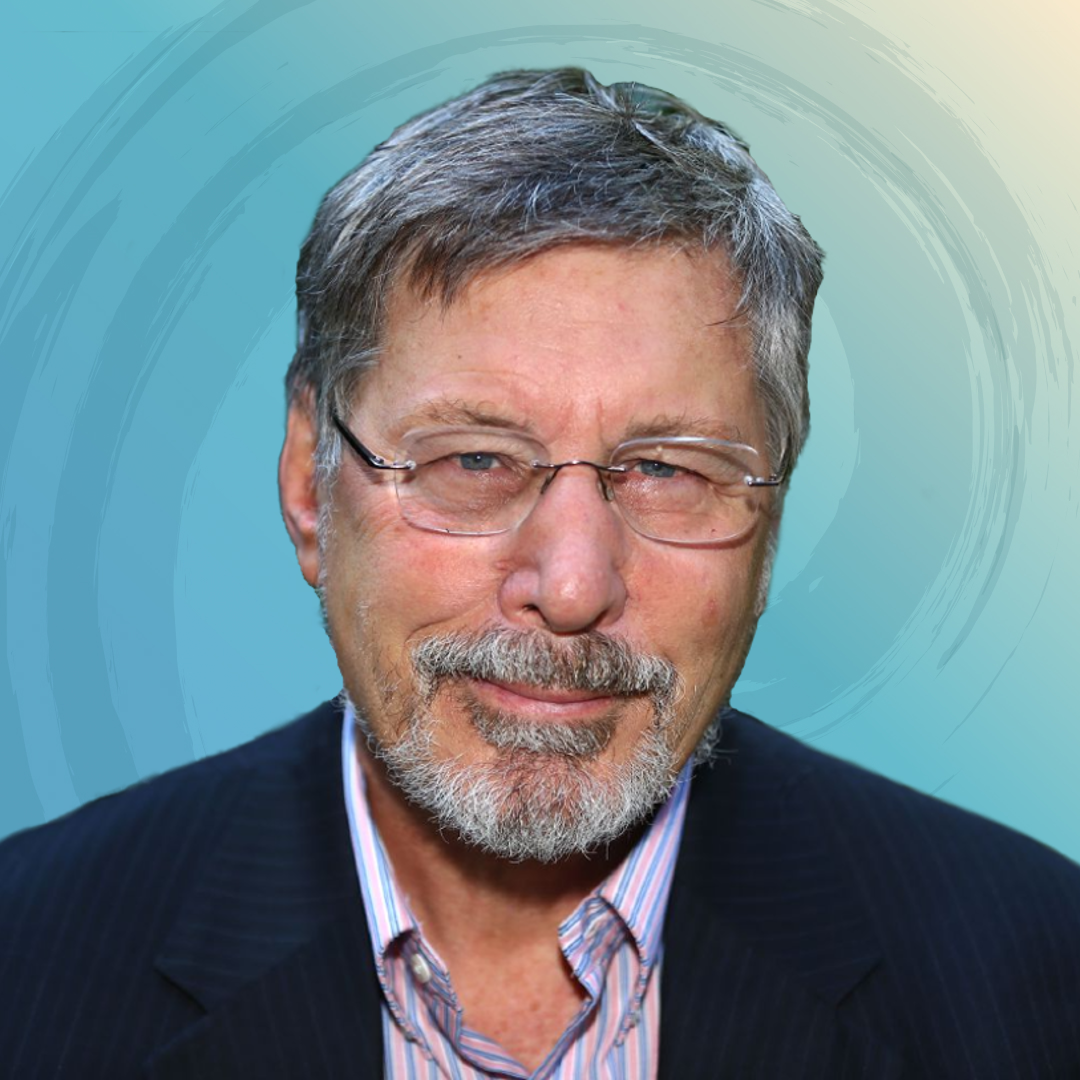 Close-up of a middle-aged man with gray hair, glasses, and a beard, wearing a dark suit and a striped shirt, against a colorful abstract background.