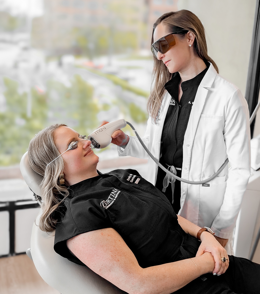 A woman receiving a dental laser treatment from a dentist in an office with a window view of trees and parking lot.