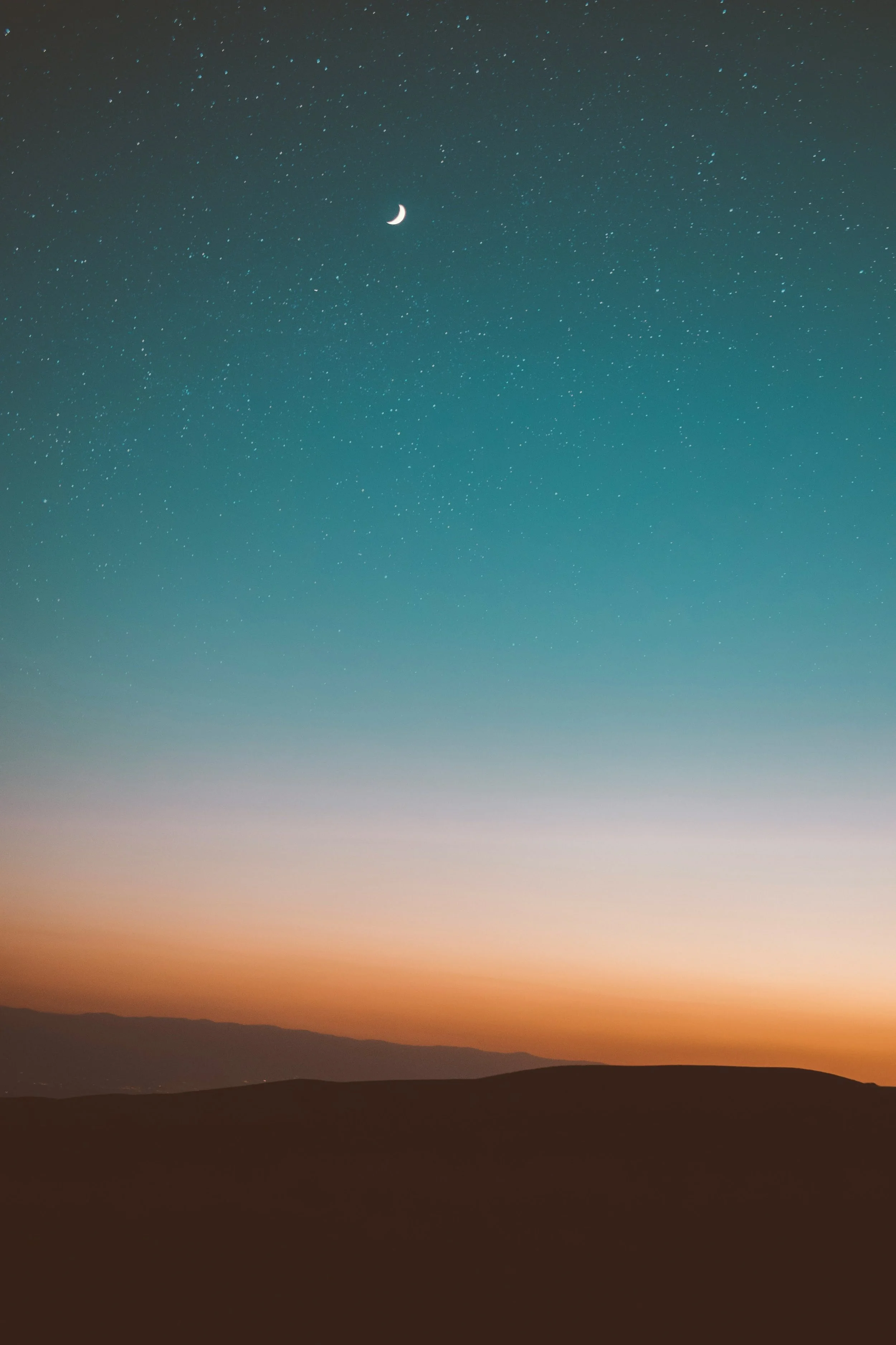 View of a starry night sky with a crescent moon above a landscape of rolling hills at sunset.