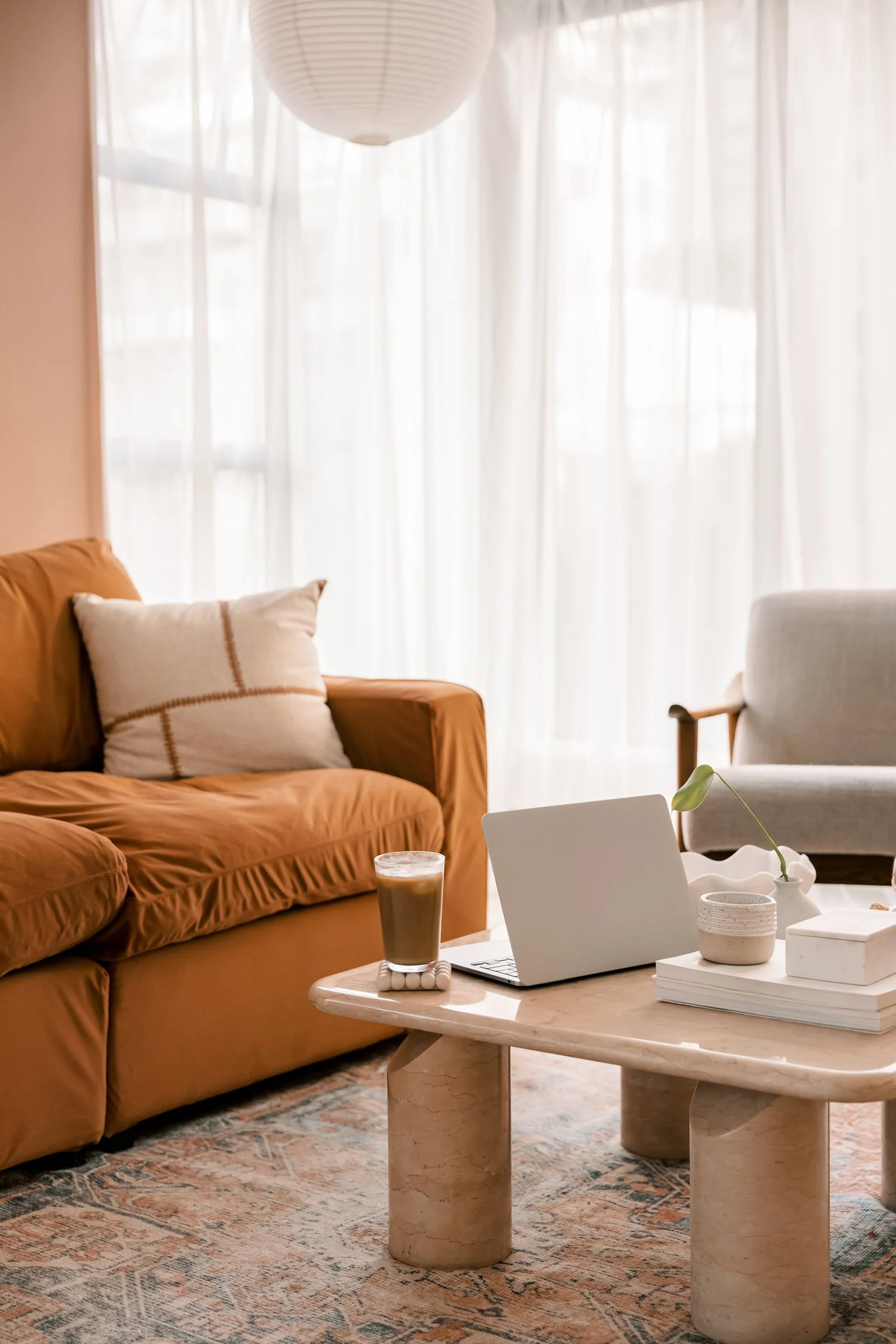 Living room with a terracotta sofa, beige armchair, marble coffee table, and white curtains in the background.