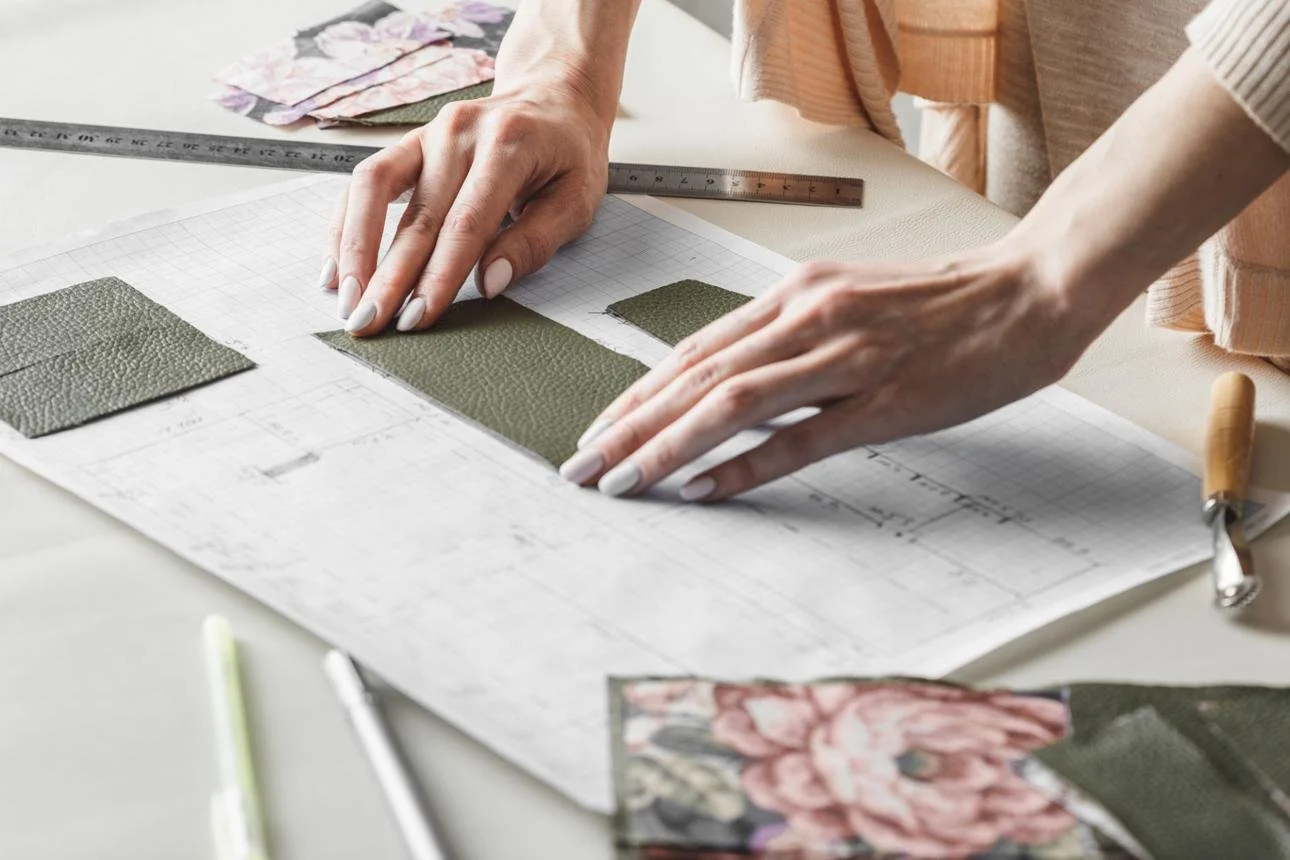 Person arranging fabric swatches on a blueprint or design plan with a ruler and tools on a work table.