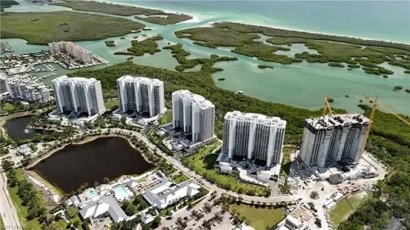 An aerial view of a coastal residential area with high-rise apartment buildings, a large pond, and green wetlands near the ocean.