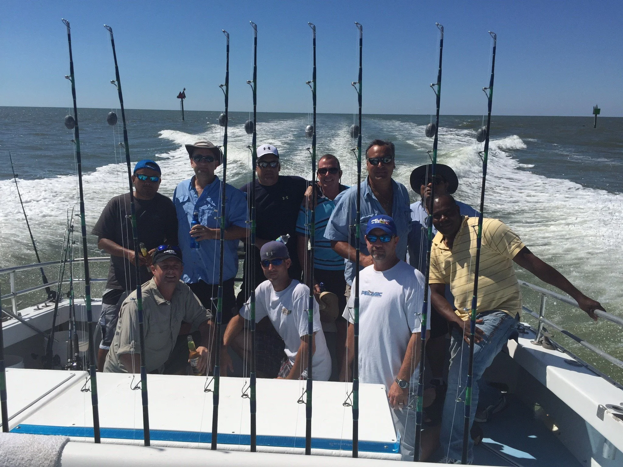 A group of men on a boat, with fishing rods, enjoying a day on the water under a blue sky.