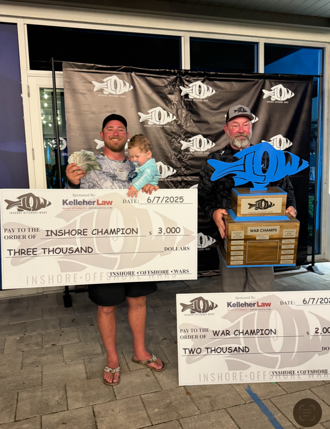 Two men and a child at an award ceremony for a fishing competition. One man is holding a large check for three thousand dollars, and the other man is holding a trophy. The background has a black banner with a fish logo and the text "INSHORE OFFSHORE 