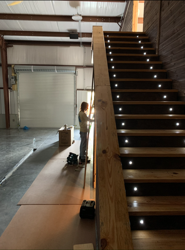 Interior view of a warehouse or workshop with a person working near a staircase with LED lights embedded in the risers.