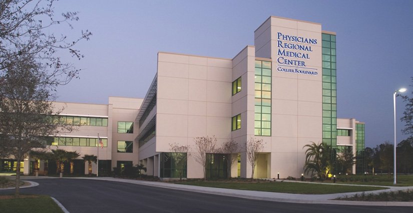 Exterior of Physicians Regional Medical Center on Collier Boulevard at dusk with a clear sky and some trees around.