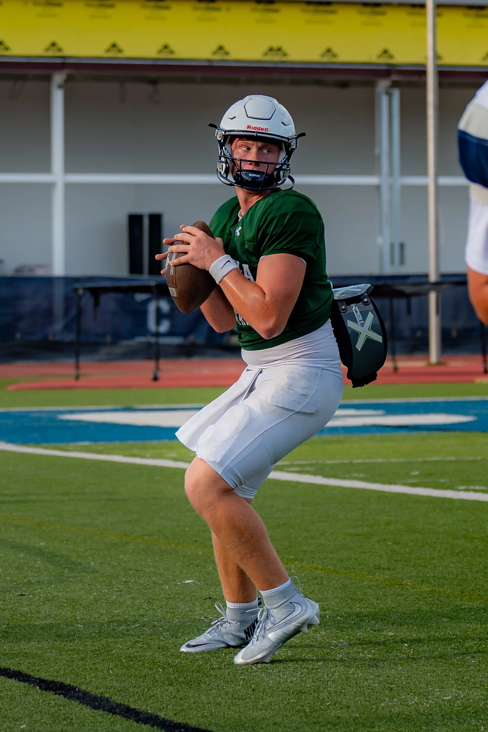 A football player in a green jersey and white shorts preparing to throw a football on a football field wearing a helmet.
