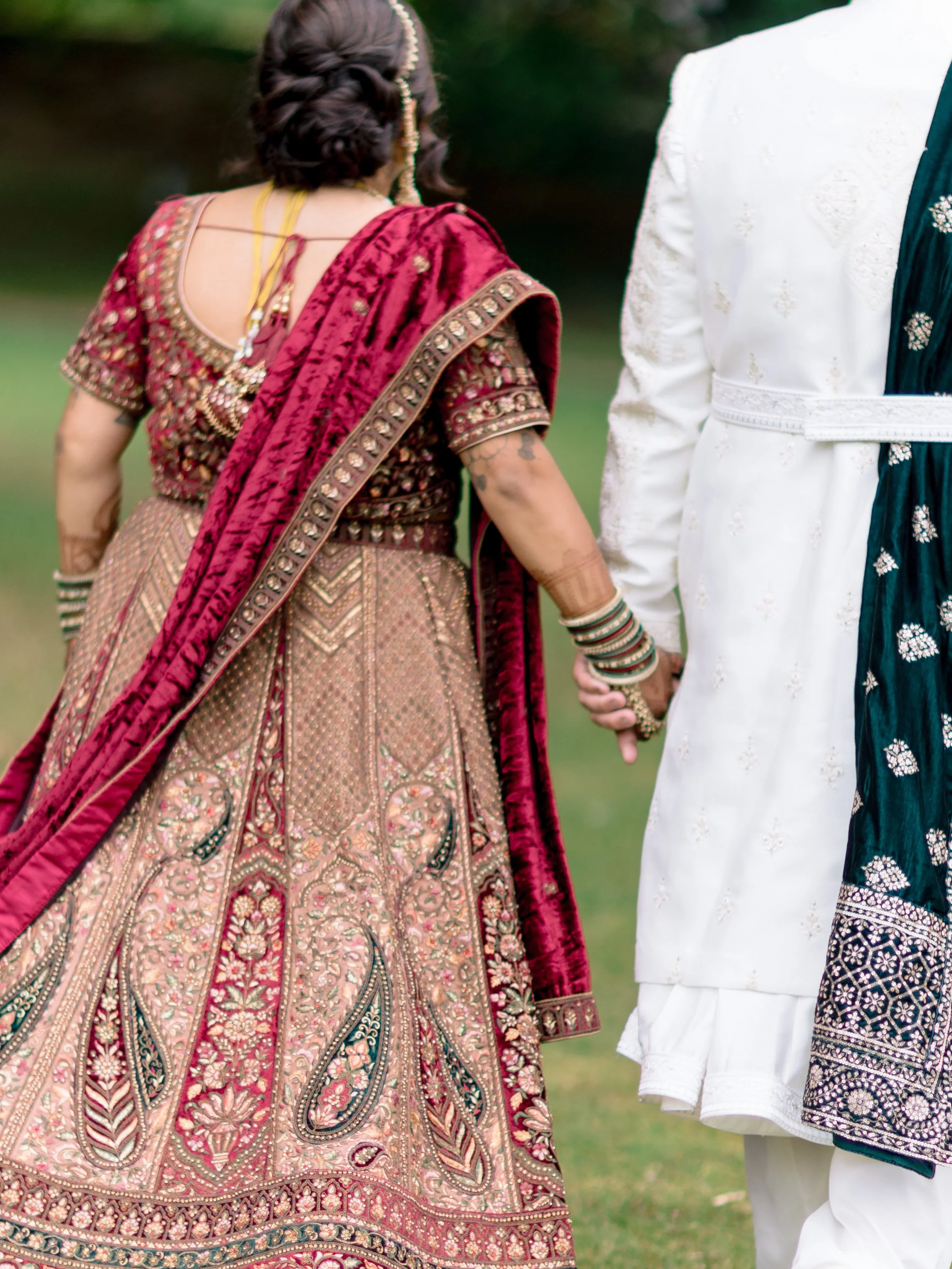 A bride and groom wearing traditional hindu wedding attire holding hands walking away