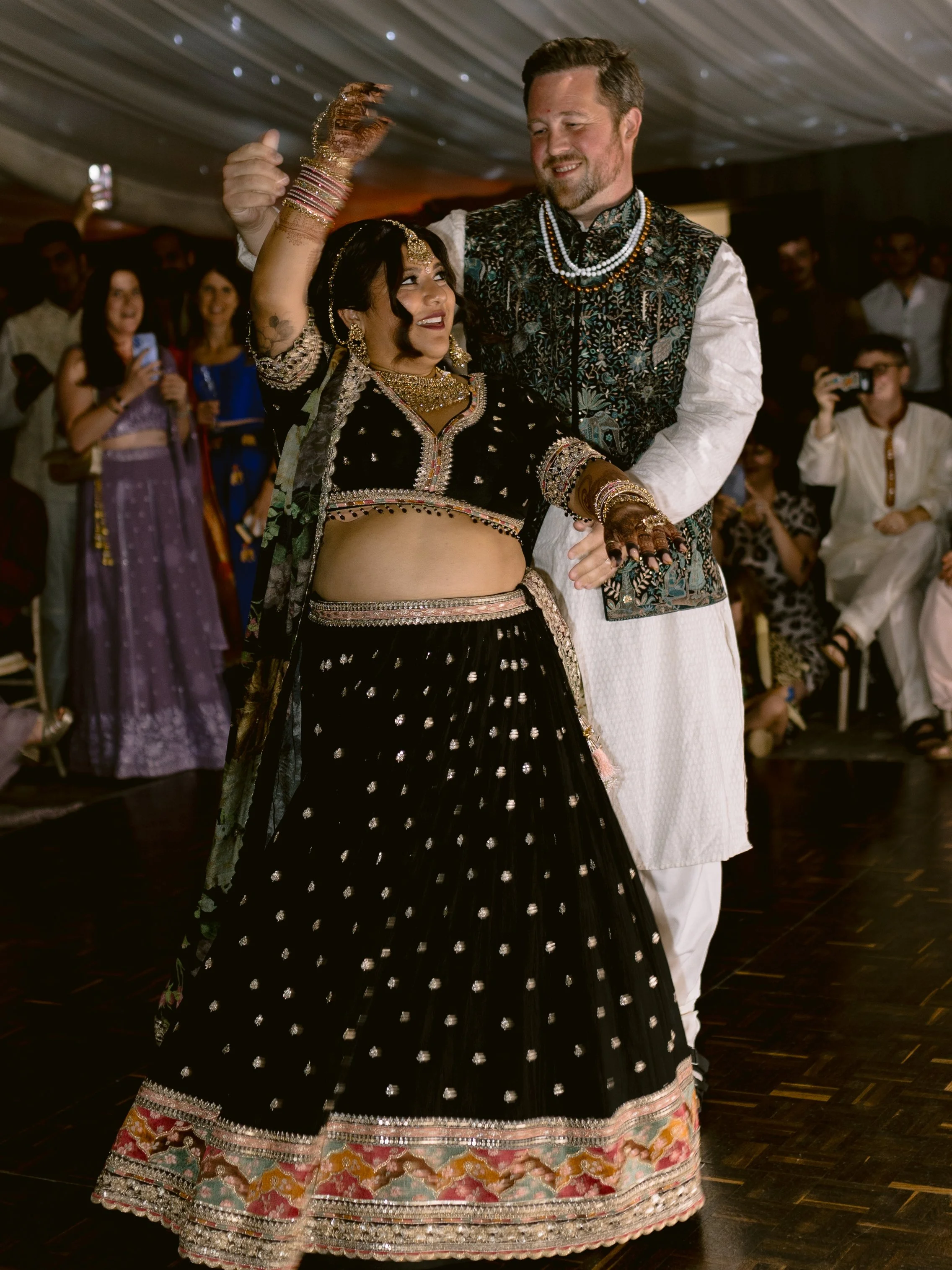 A bride and groom in south east asian wedding attire during their first dance in the marquee at Oakley Hall
