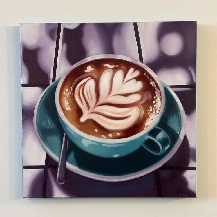Painting of a coffee cup with latte art on top, sitting on a saucer with a spoon, on a tiled surface with blurred background.