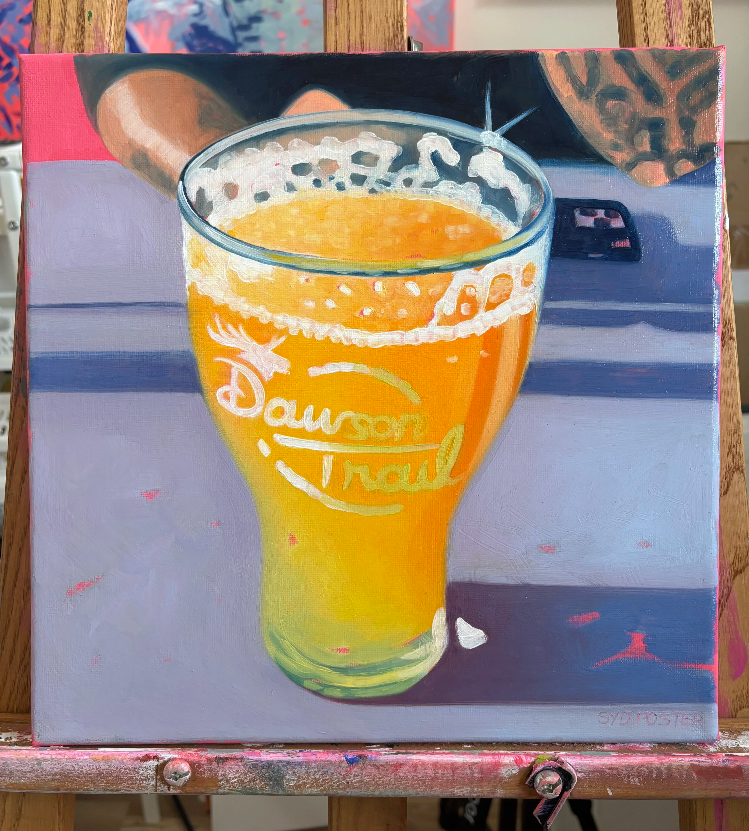 Painting of a glass filled with orange juice, with a basketball on top and a tattooed arm in the background. The painting is signed 'SYD FOSTER' at the bottom right corner.