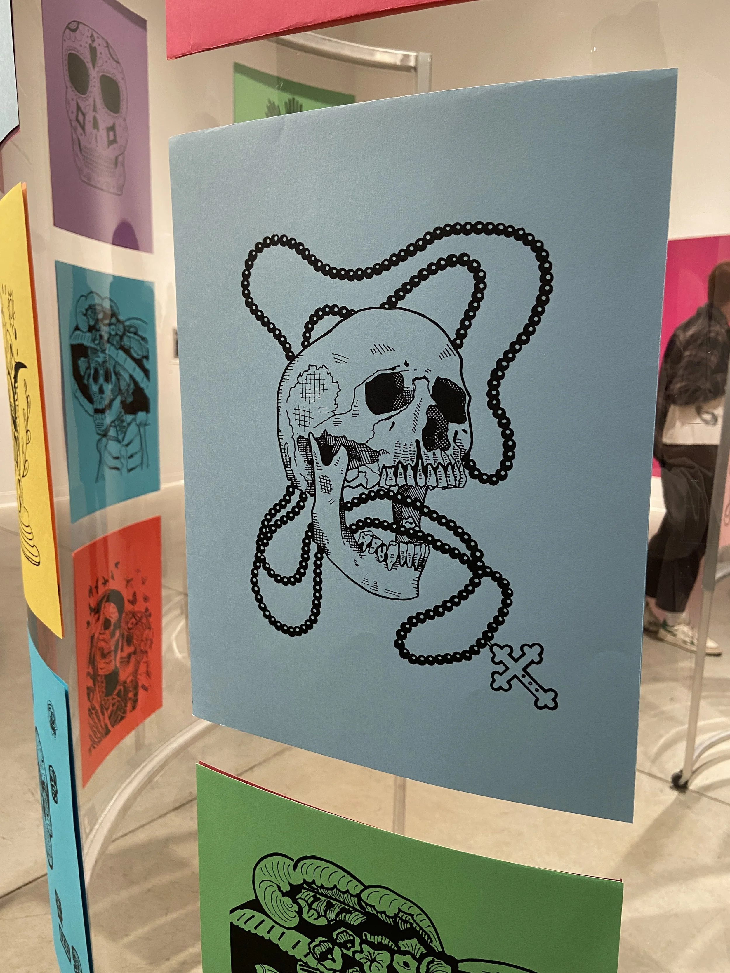 Colorful display boards with illustrations, including a skull with a beaded chain and a cross, at an indoor event.