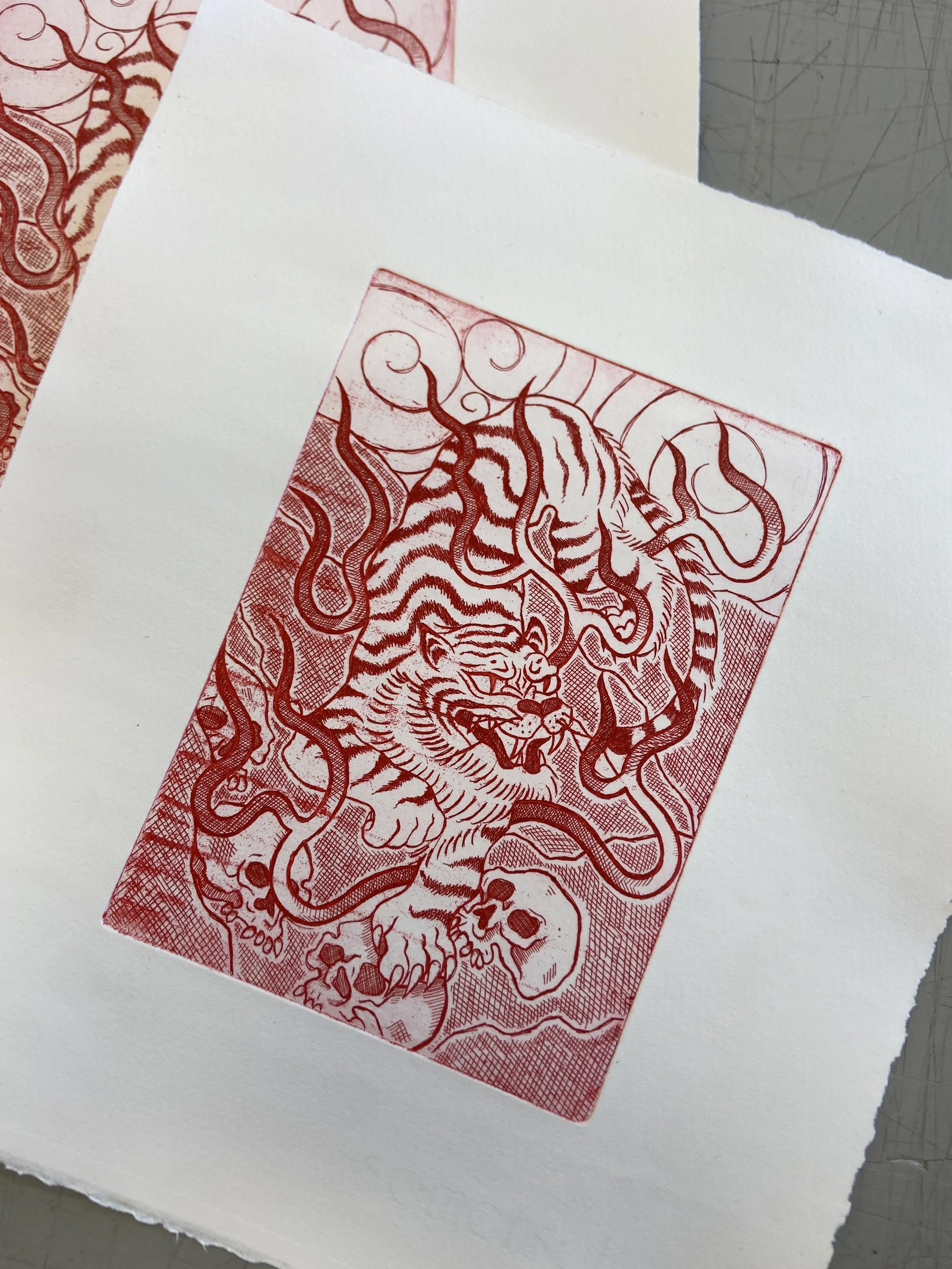 A close-up photograph of a red illustrated tiger on a piece of paper, placed on a white surface with additional paper nearby.