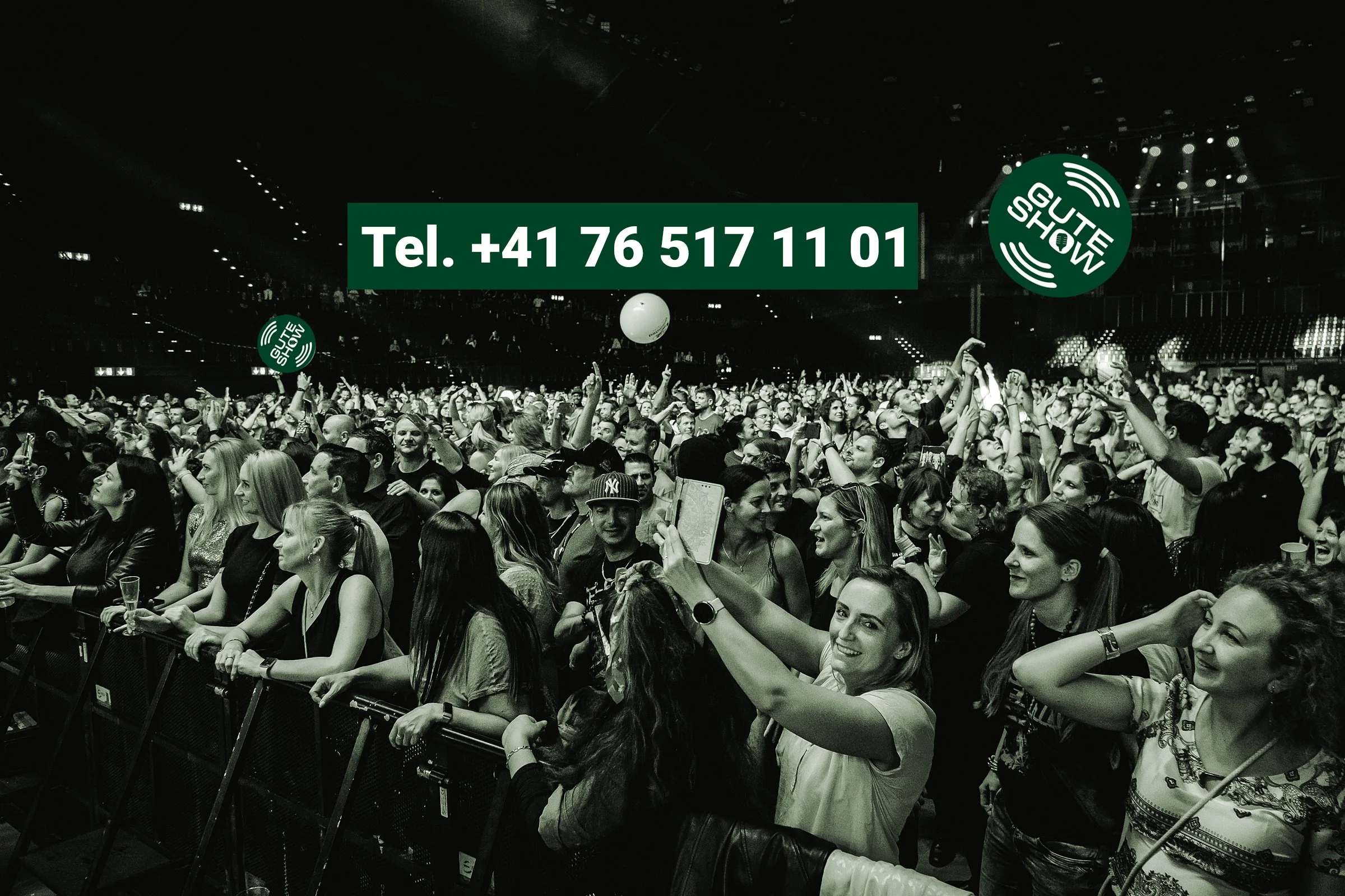 Menschen beim Konzert, würden im Publikum tanzen und Fotos machen, mit einem großen Banner mit Telefonnummer und 'Gute Show'-Logo