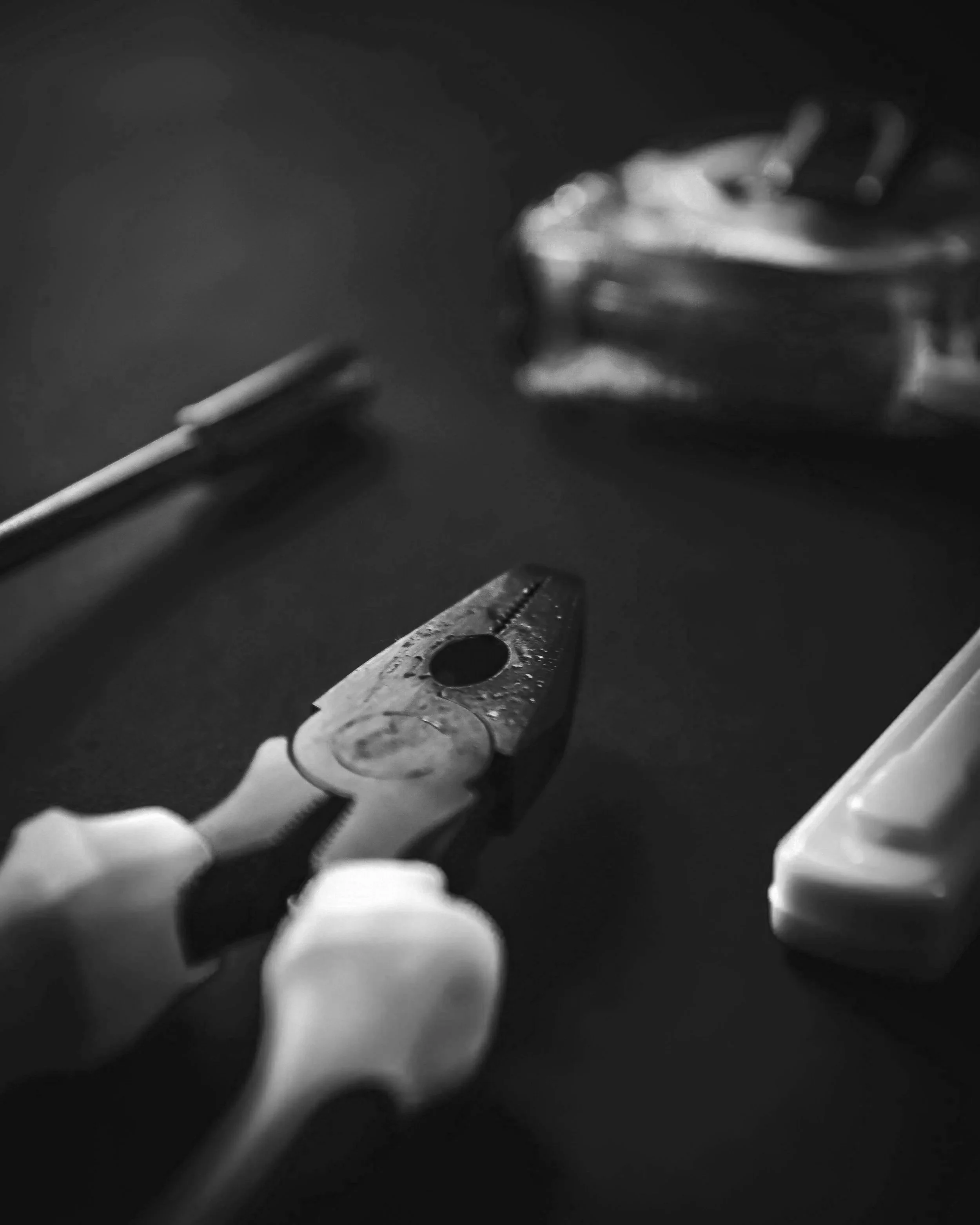 Close-up of a lit cigarette and a pair of pliers on a dark surface.