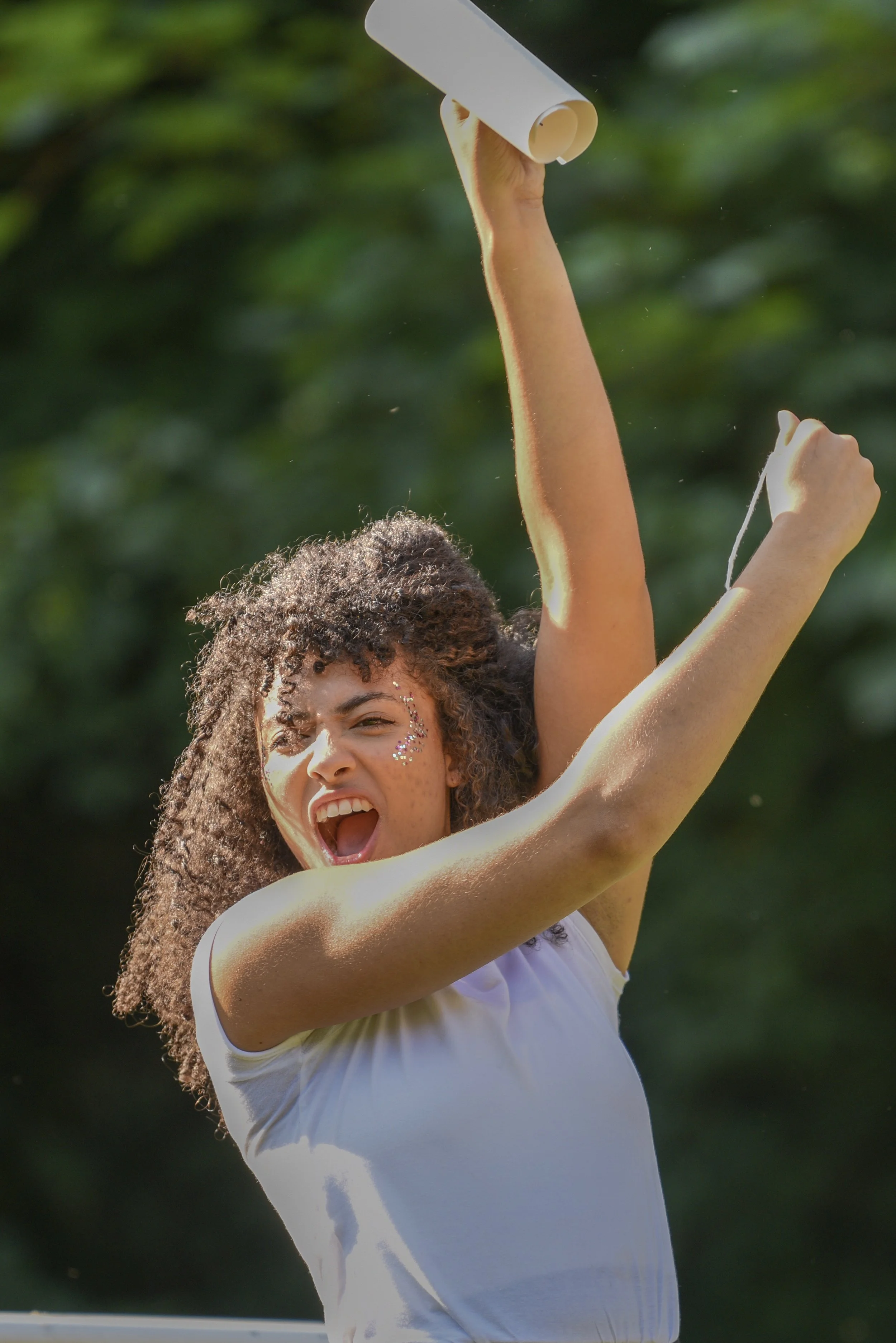 A Midsummer Night's Showcase, 2021. A woman with glitter on her face enthusiastically holds a piece of scroll in the air.