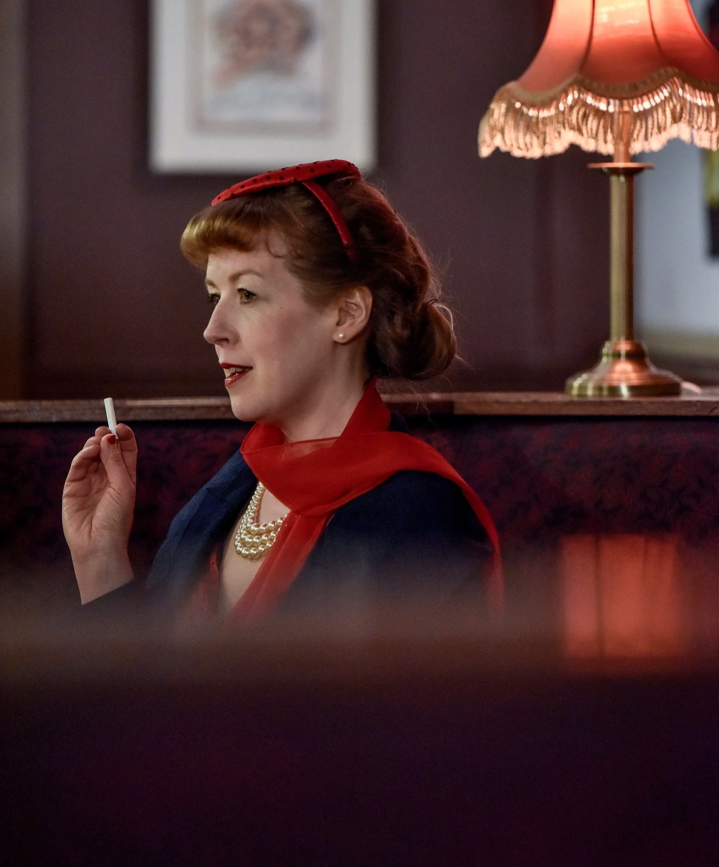 Whodunnit at the Coliseum, 2021. A glamorous woman in 1950s dress sits in a theatre bar and smokes a cigarette.